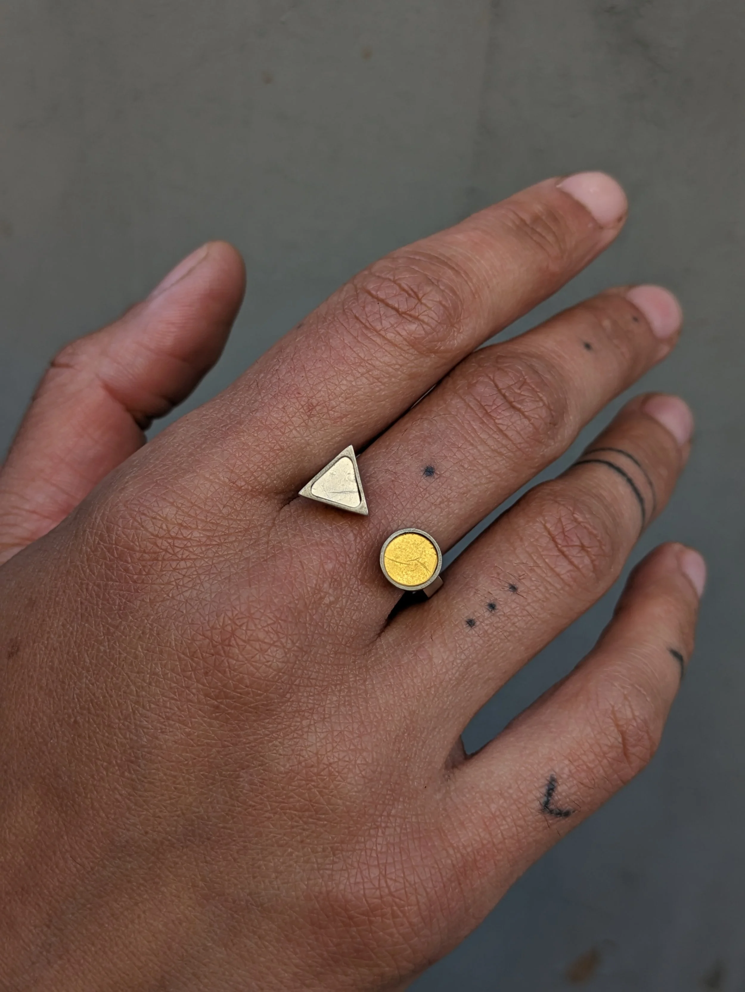 Main avec une bague en mosaïque contre une surface grise.