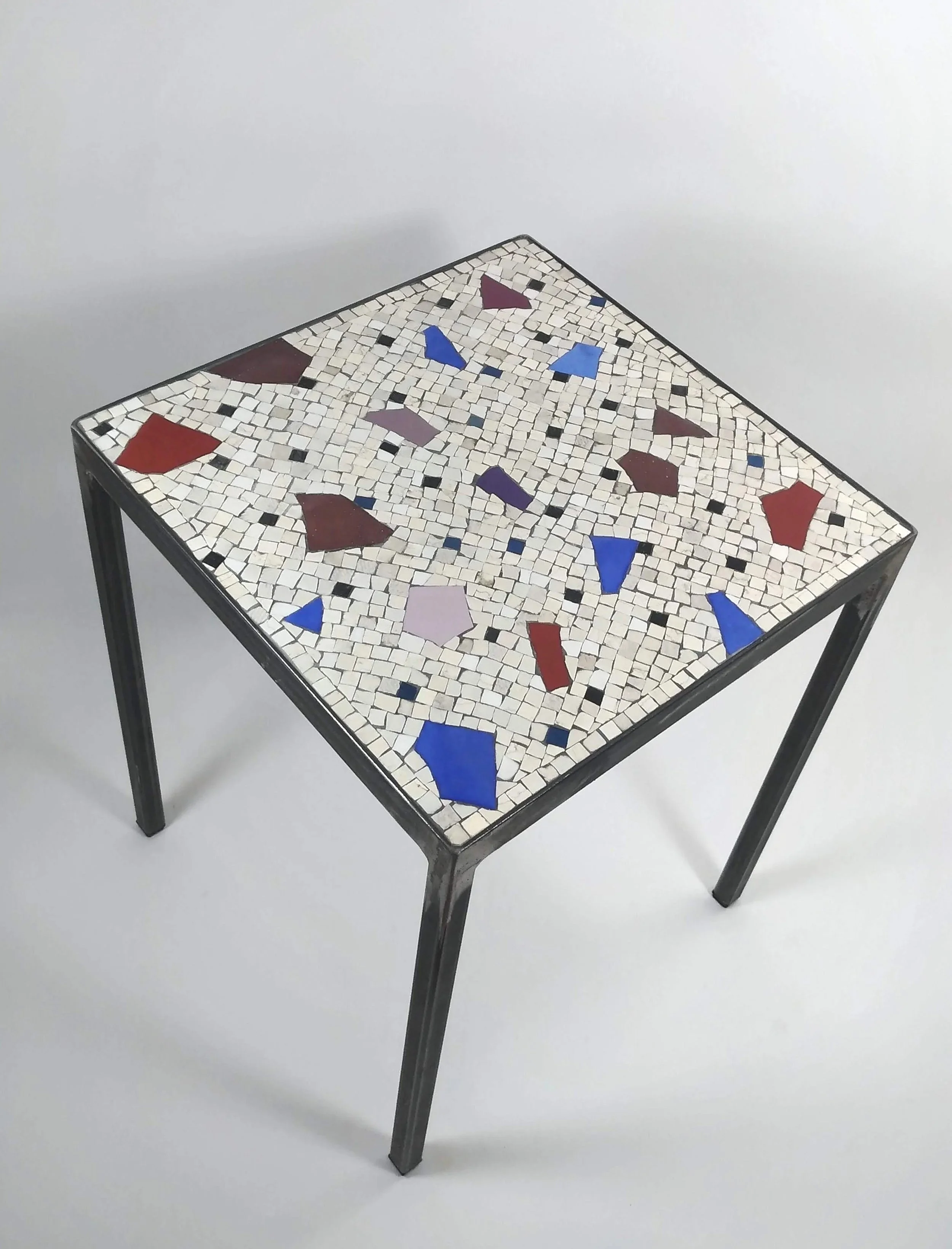 Table en métal avec surface en mosaïque de petits carreaux de différentes couleurs dont du blanc, rouge, violet et bleu