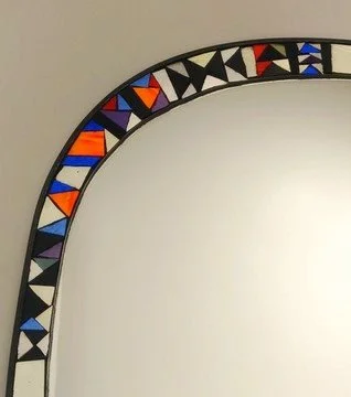 Un miroir en mosaïque avec un cadre orné de formes géométriques colorées.