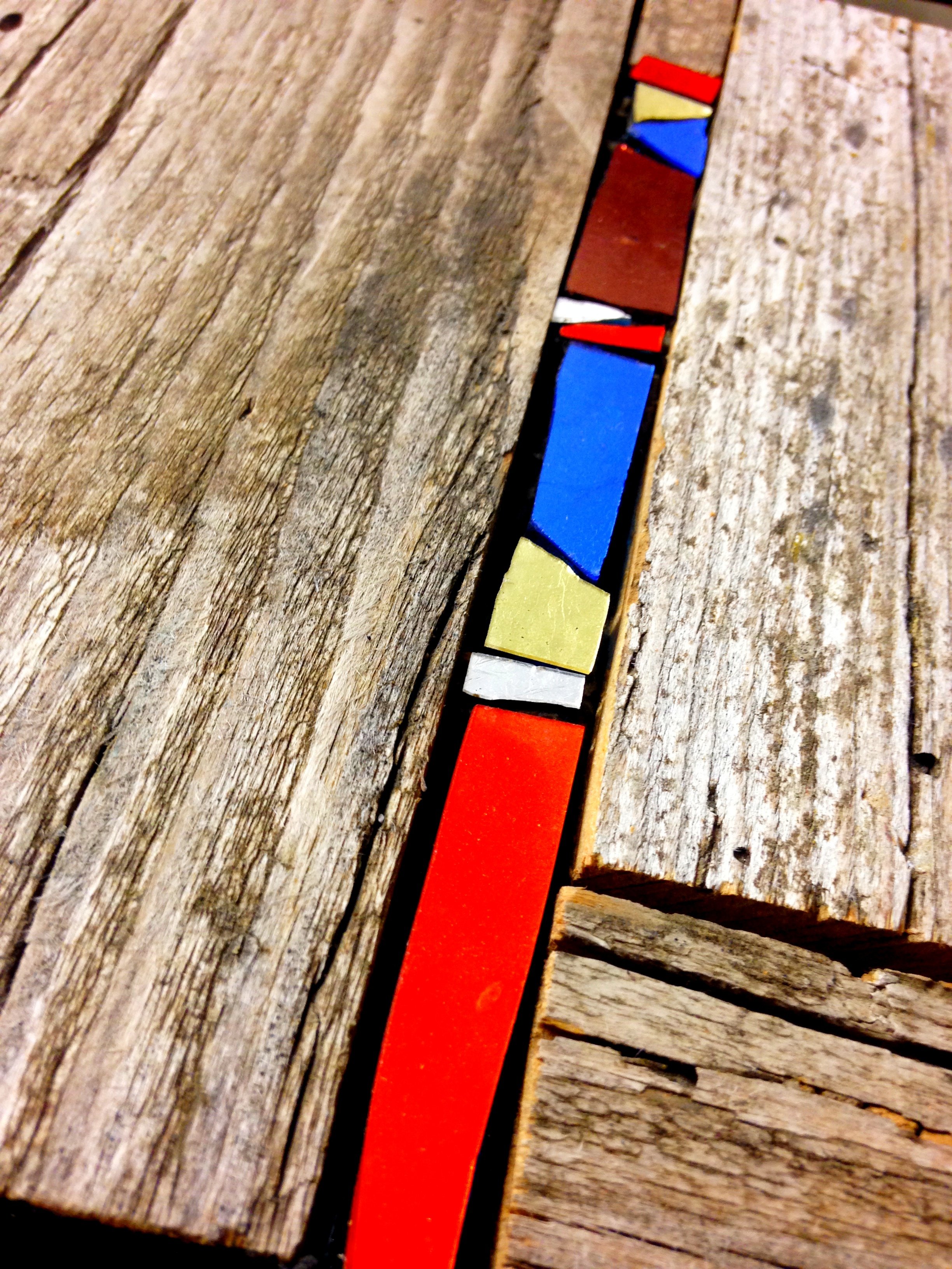 Bijou mural en mosaïque, un long plateau en bois avec une ligne de pièces de jeu de société colorées, notamment rouge, jaune, blanc, bleu et orange, disposées sur la surface.