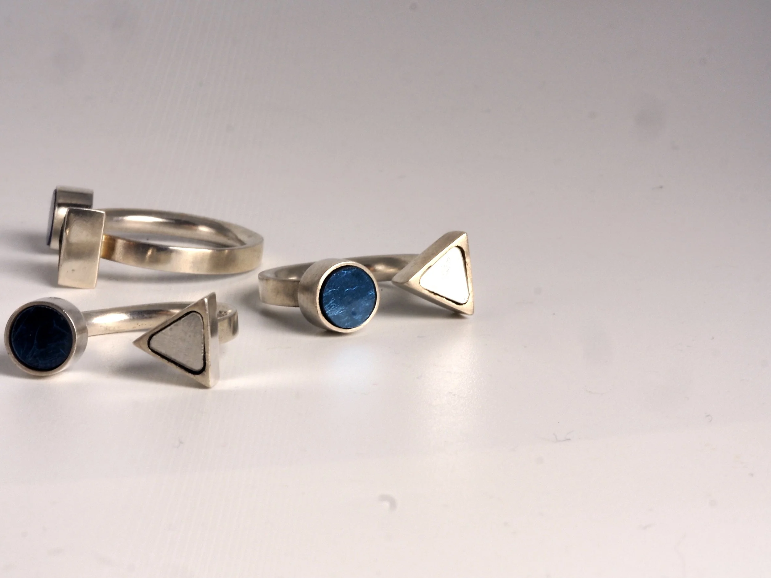 Bague en mosaïque et en métal avec pierres bleues et formes géométriques, disposés sur une surface blanche.
