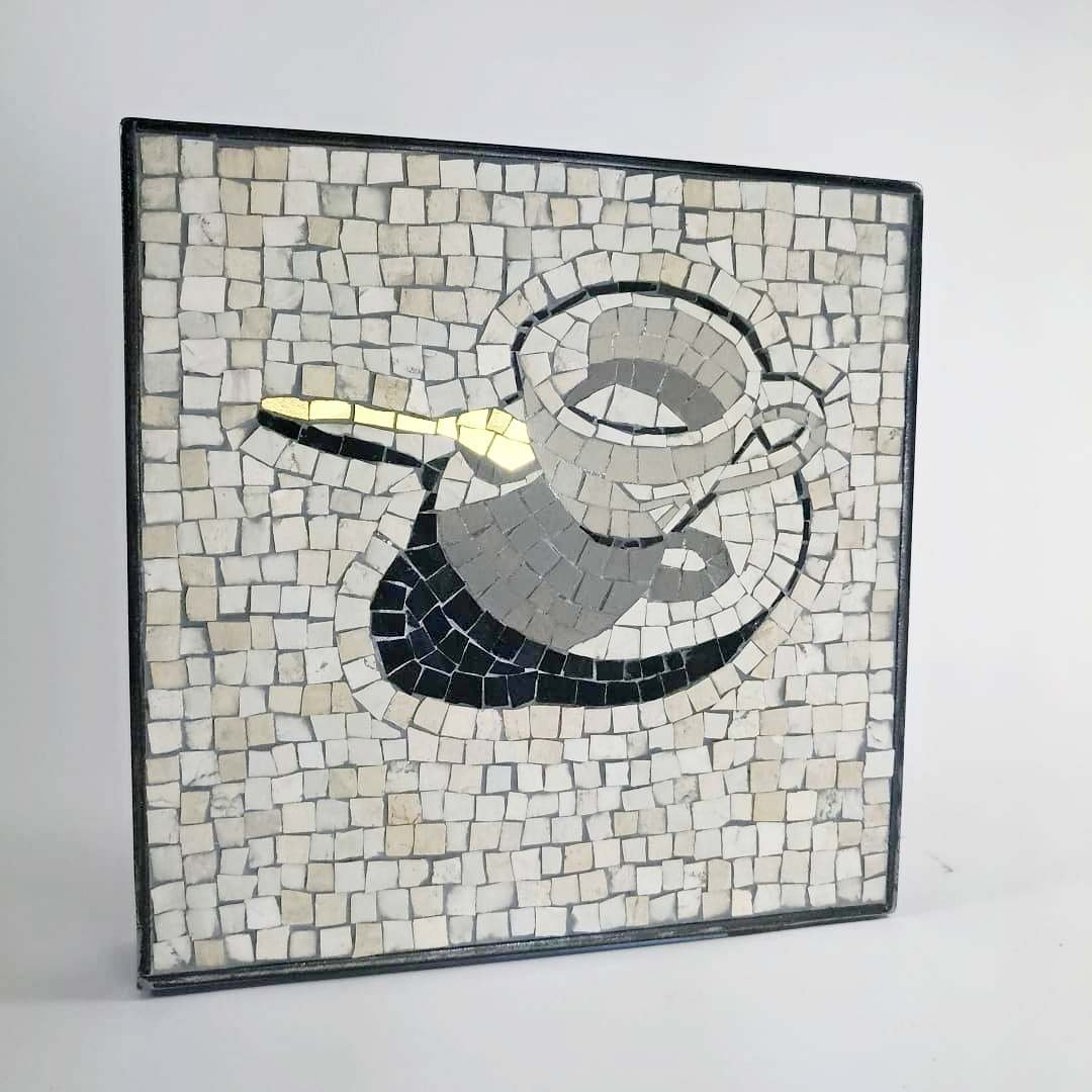 Mosaïque représentant une tasse à cappuccino avec une cuillère et une cuillère à café, composée de petits carreaux de différentes nuances de blanc, noir et gris.