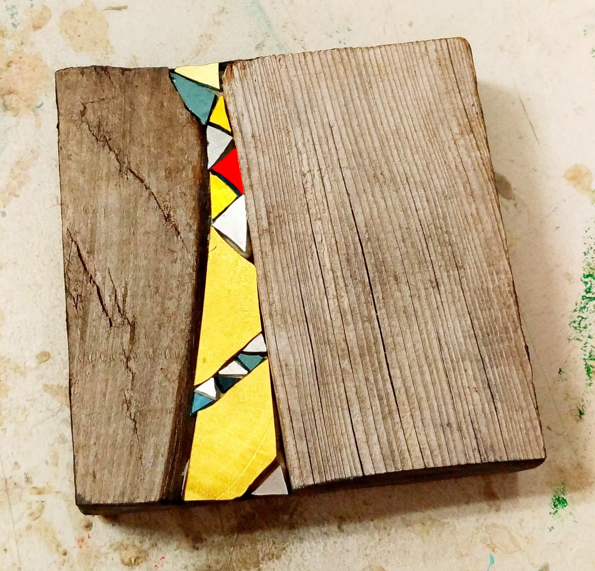 Trois morceaux de bois avec des motifs colorés en bas, posés sur une surface beige, avec des taches de peinture.