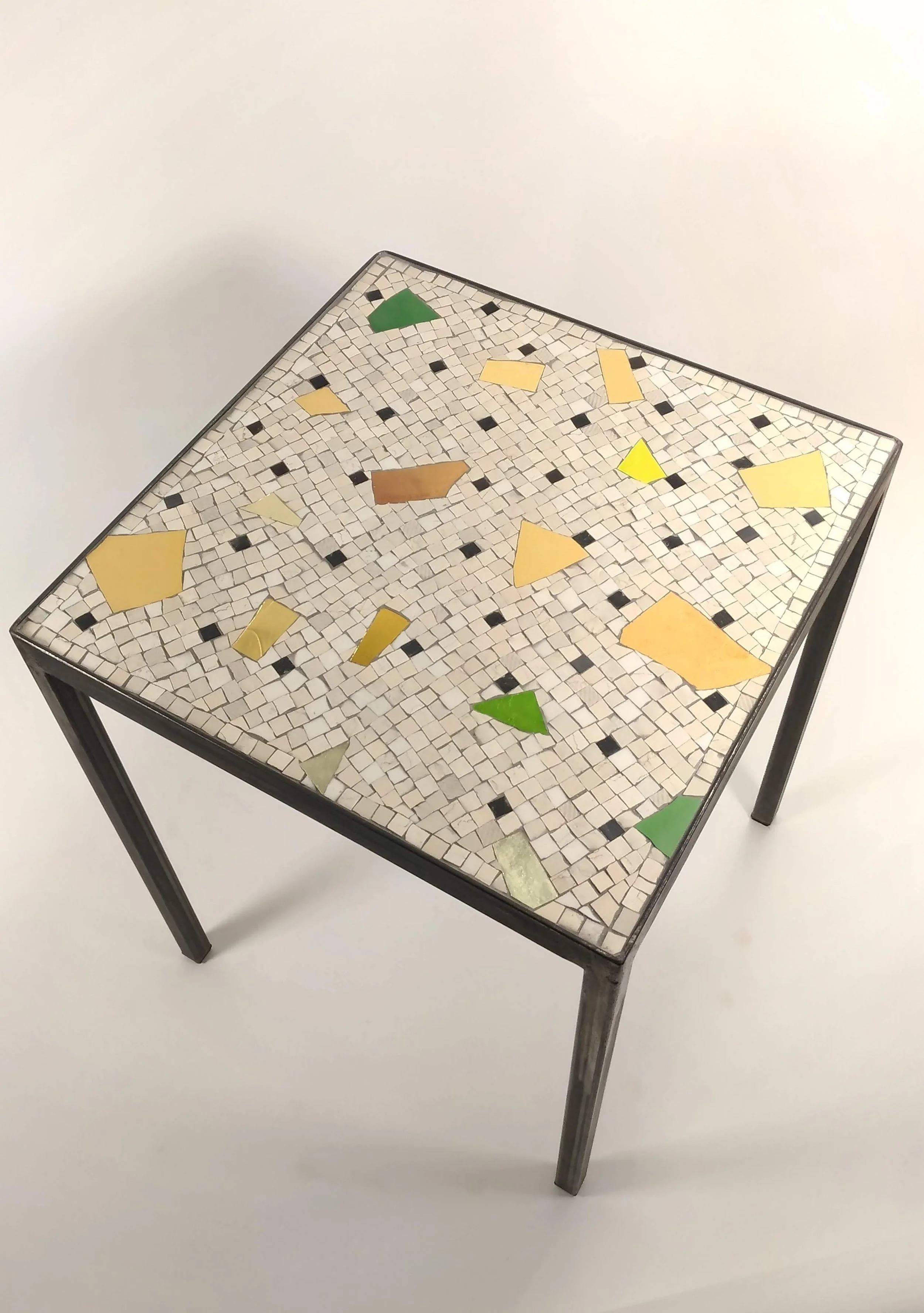 Une table avec un dessus en mosaïque de petits carreaux blancs, noirs et colorés, présentant un design de mosaïque artistique.