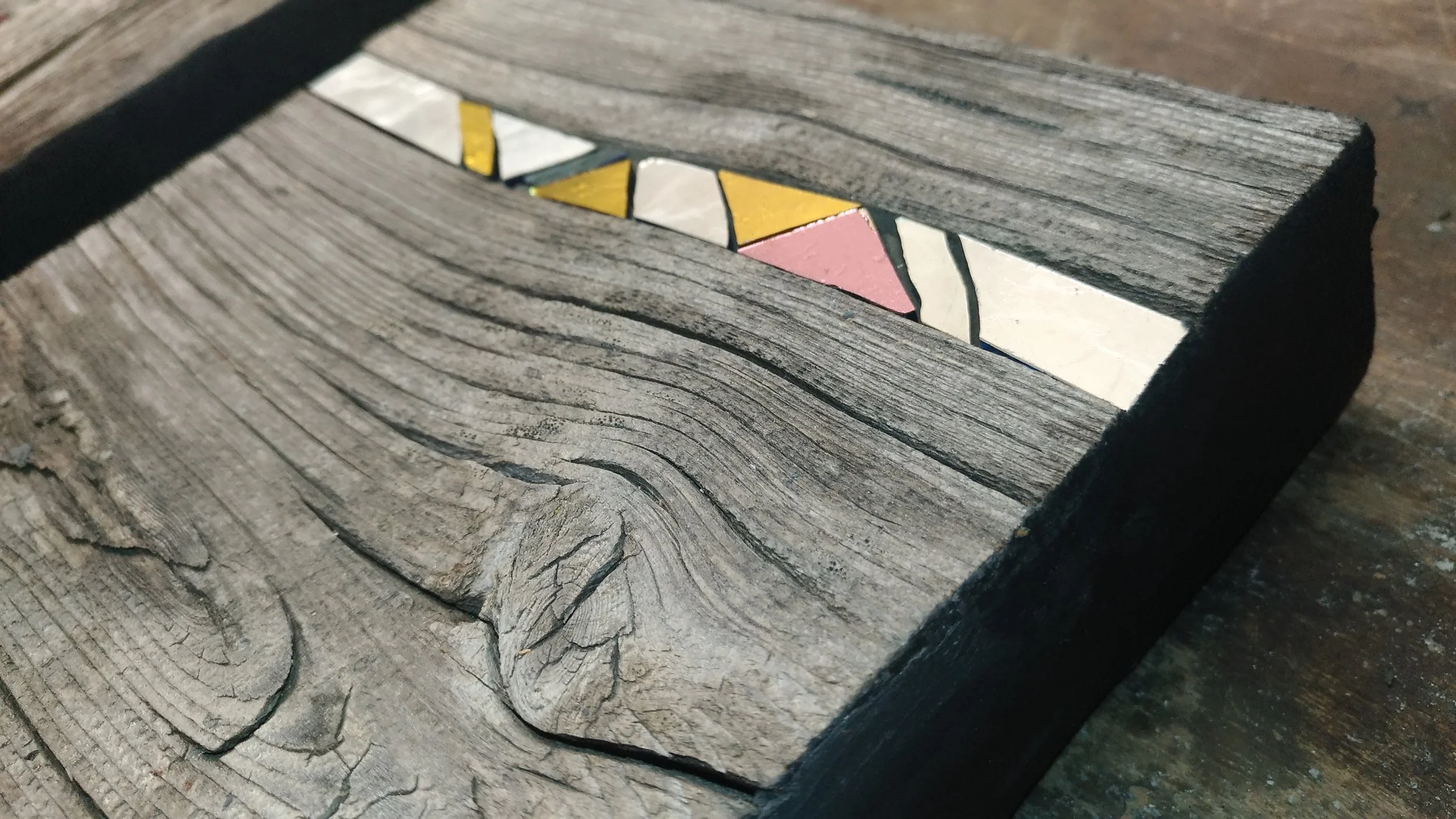 Une mosaïque colorée en formes géométriques sur un élément en bois délavé, placé sur une surface en bois.