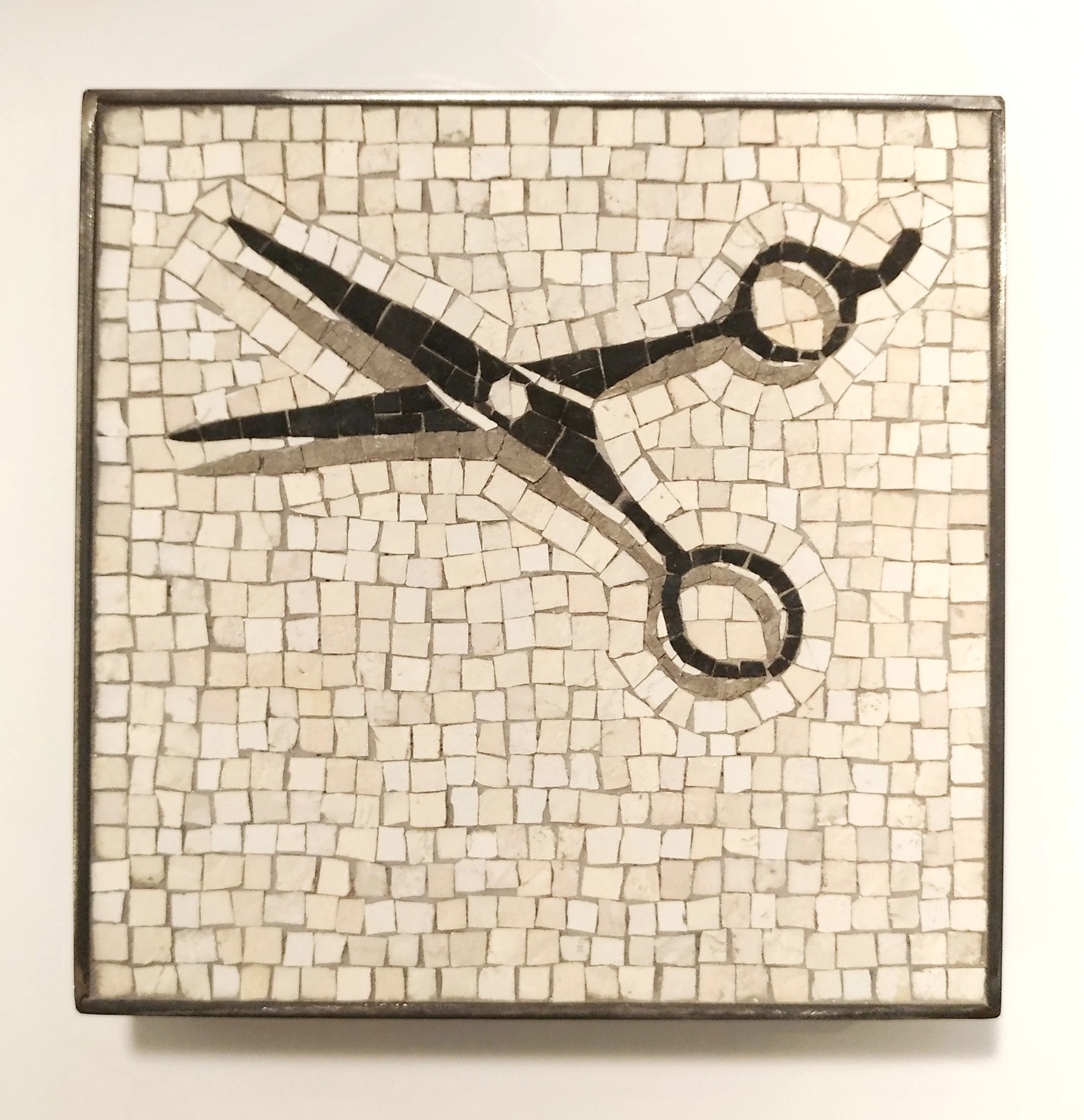 Mosaïque représentant une ciseau en noir et blanc, encadrée dans une boîte en métal.