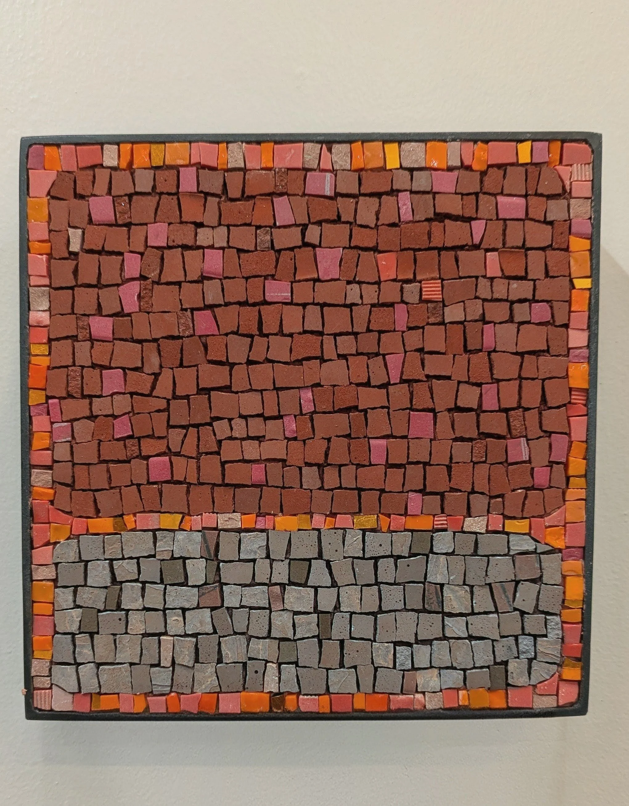 Tableau mural en mosaïque avec différentes sections de couleurs et textures, comprenant des tuiles rouges, roses, oranges, gris clair et foncé.
