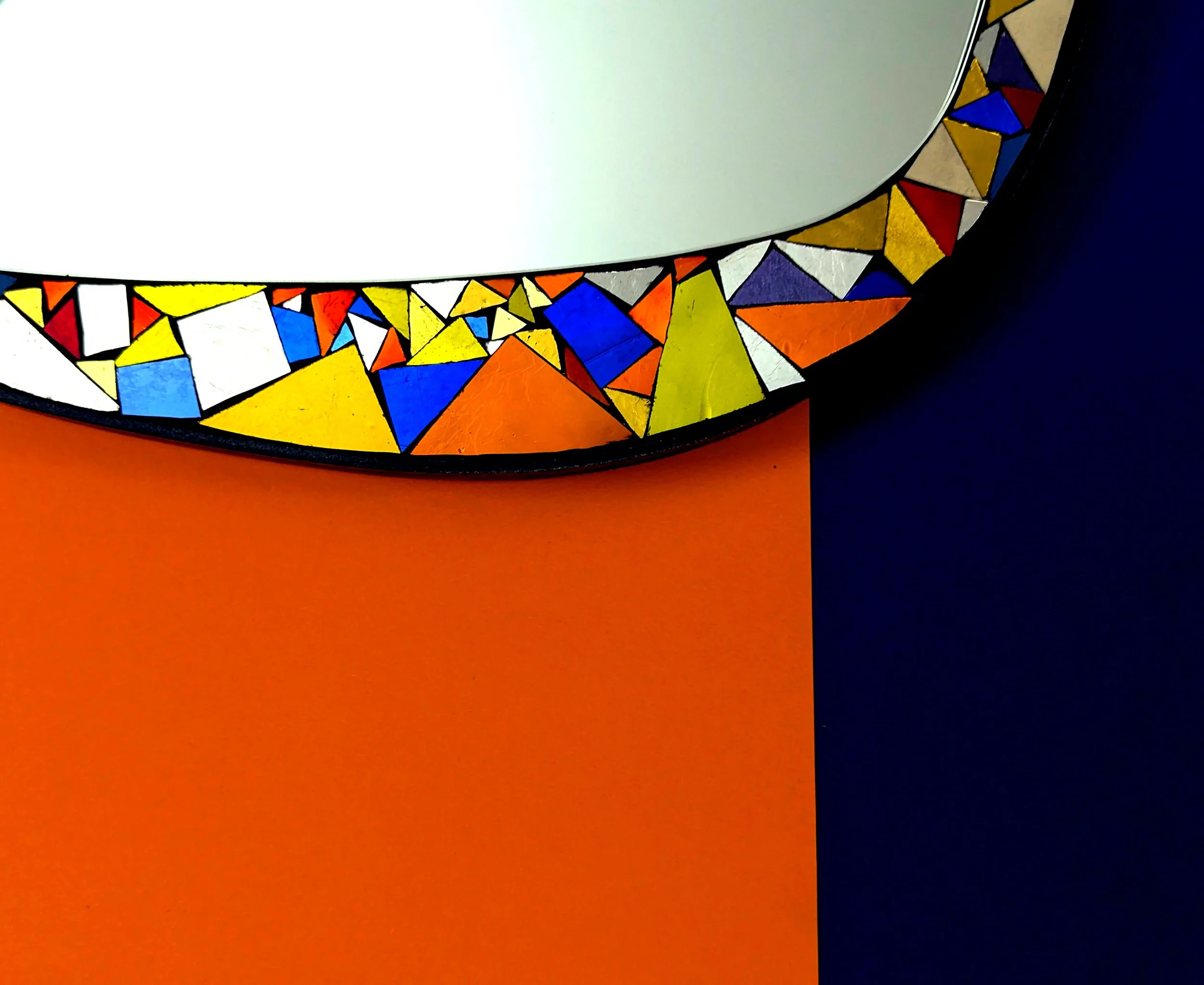 Un miroir, encadré d'un cadre coloré avec des formes géométriques en rouge, jaune, bleu et blanc, placé au-dessus d'une surface orange.