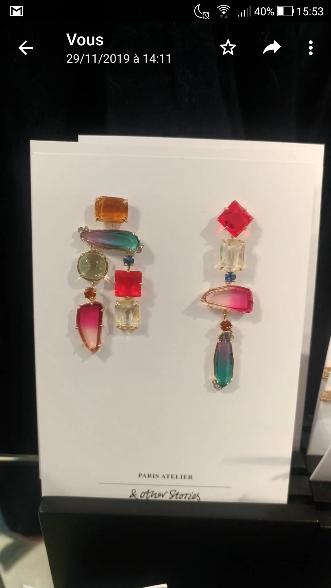Deux boucles d'oreilles suspendues avec des pierres précieuses colorées sur un fond blanc, avec le texte "PARIS ATELIER & other Stories" en dessous.