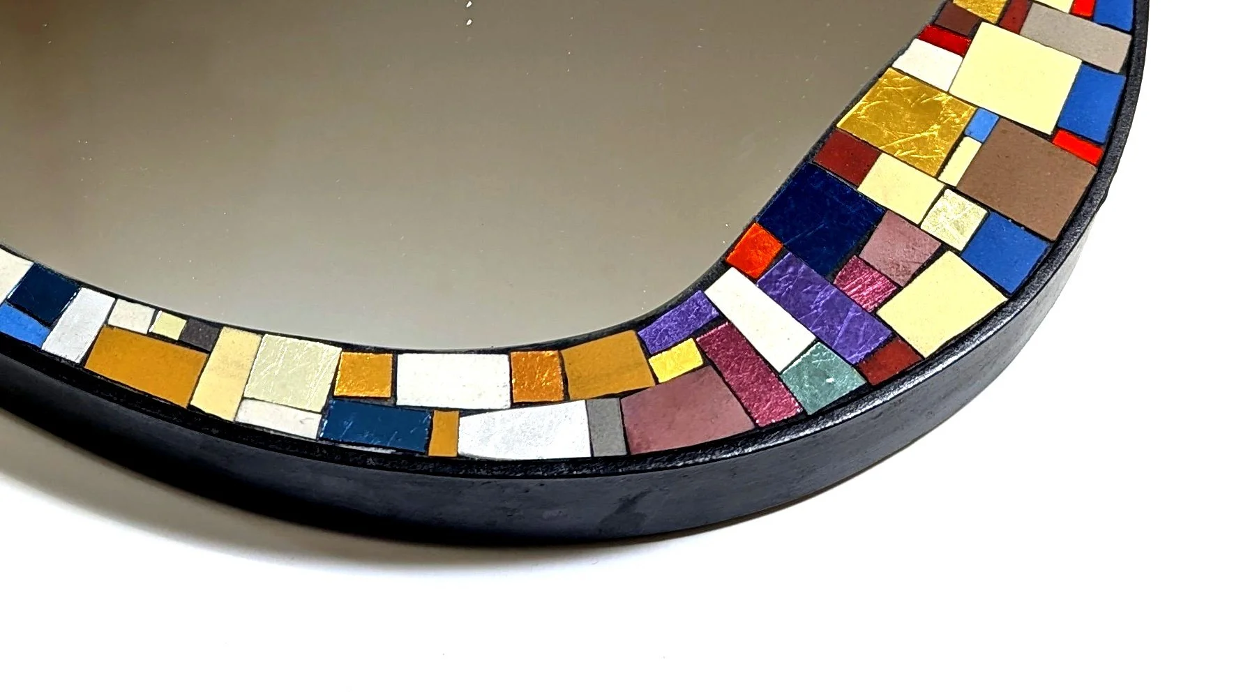 Miroir rond avec cadre décoré de petits mosaïques colorées, semblant en verre ou en céramique, disposées en rangées de couleurs diverses.
