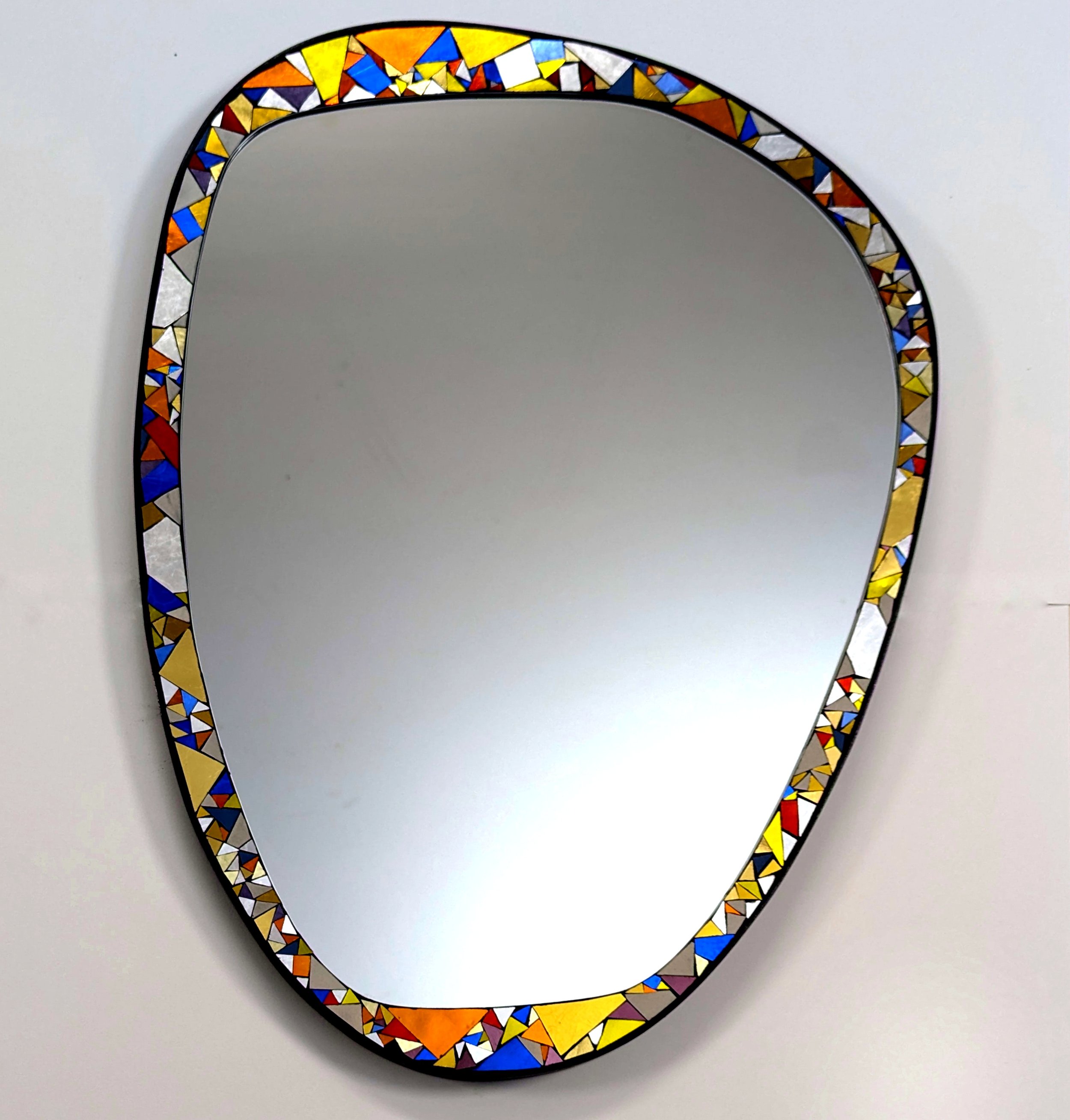 Miroir avec cadre en mosaïque de petits triangles colorés, posé sur fond blanc.