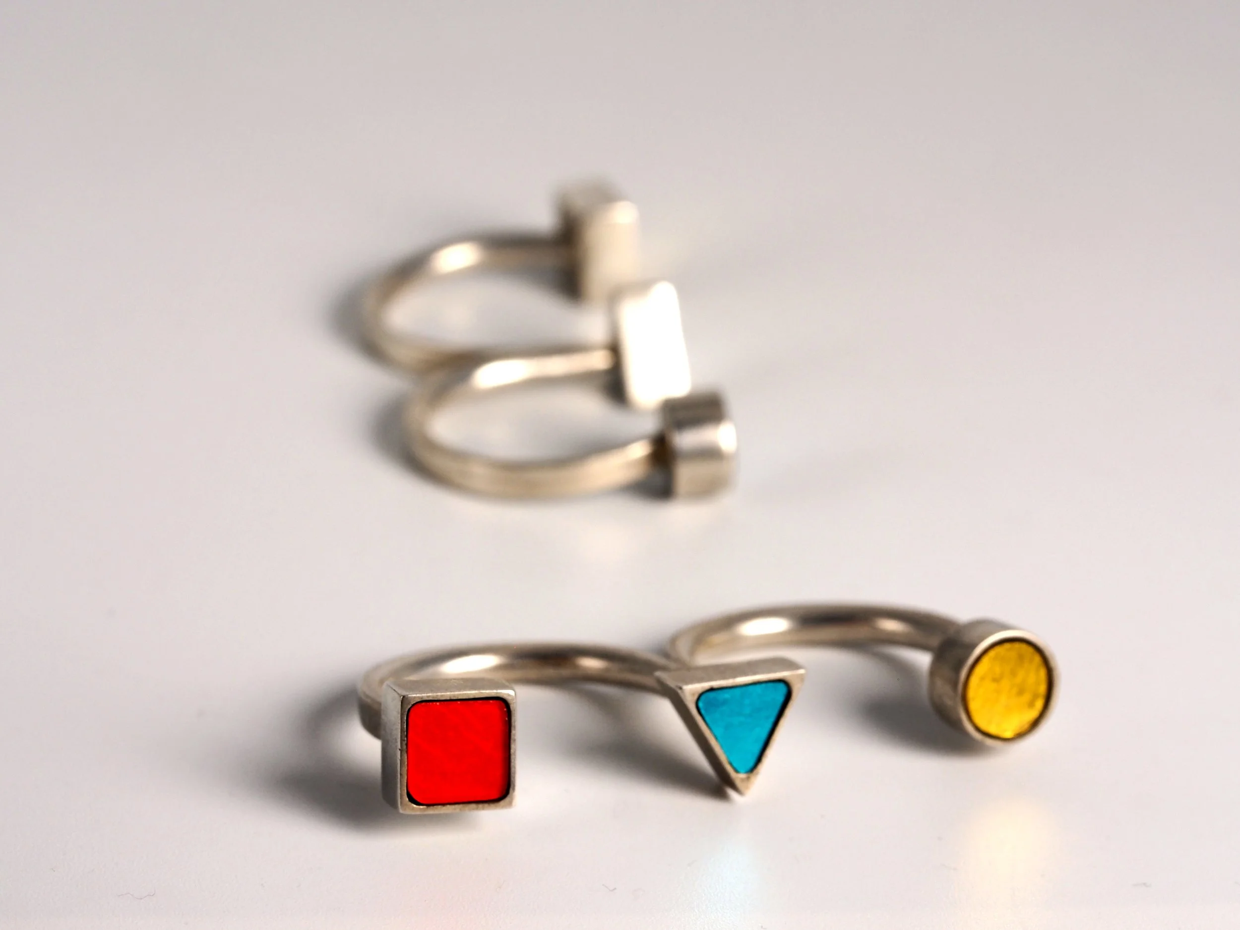 Bagues doubles en mosaïque avec formes colorées (rouge, bleu, jaune) sur un fond blanc.
