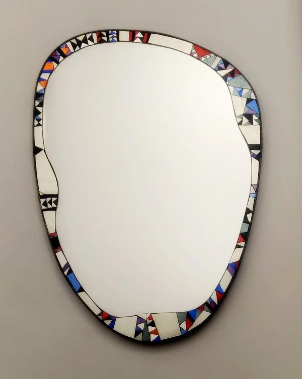Un miroir en mosaïque avec un cadre en forme irrégulière, décoré de petits carrés et triangles colorés.