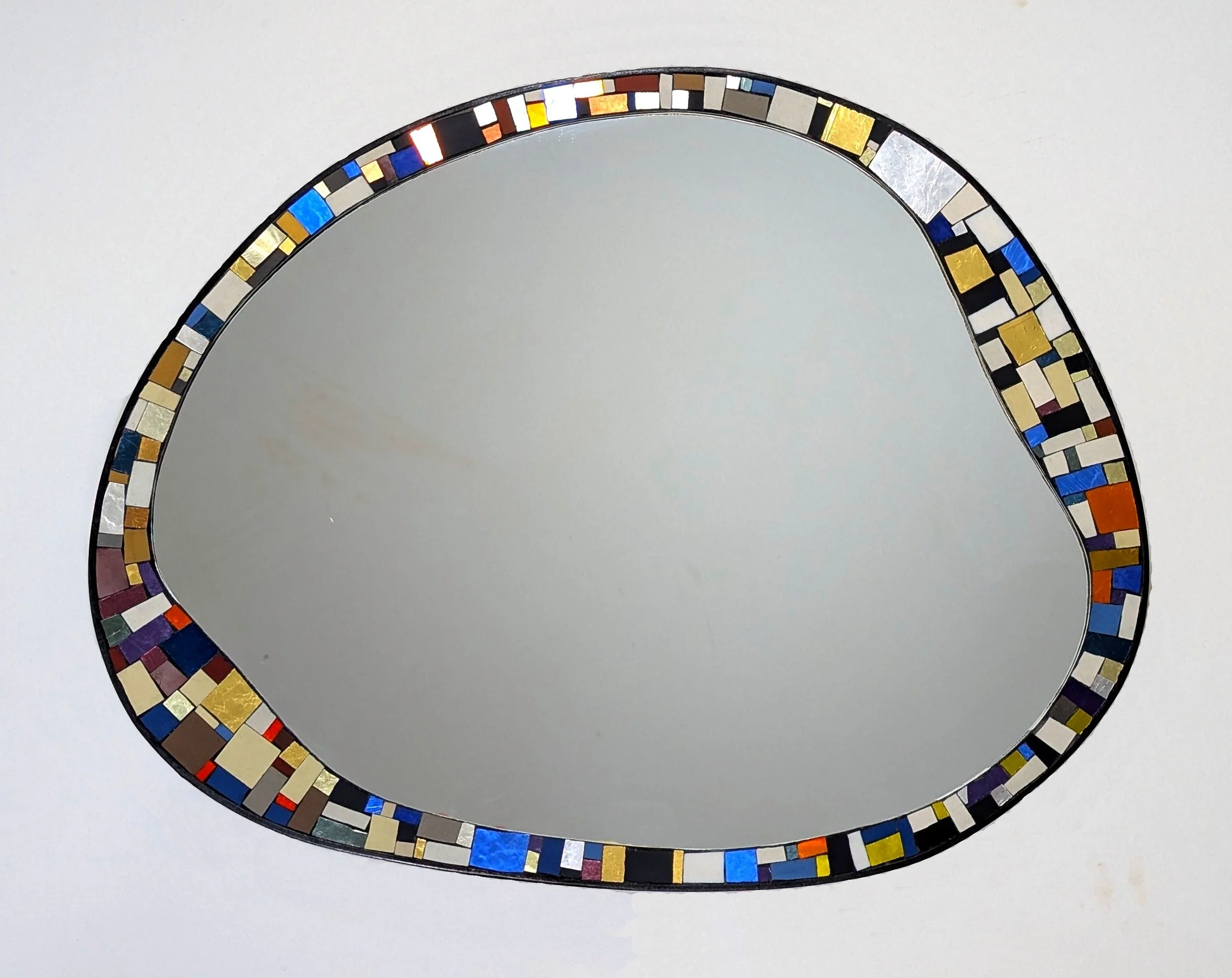 Un miroir placé sur une surface blanche, entouré d'une bordure mosaïque colorée avec des carrés en verre dans diverses teintes