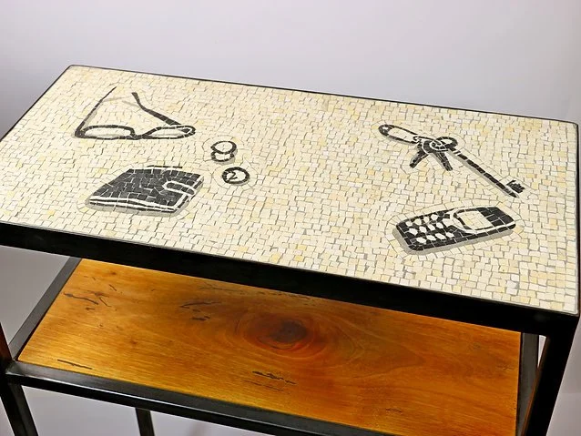 Table avec mosaïque représentant des objets personnels comme des lunettes, une montre, une clé, des boutons et un téléphone portable.