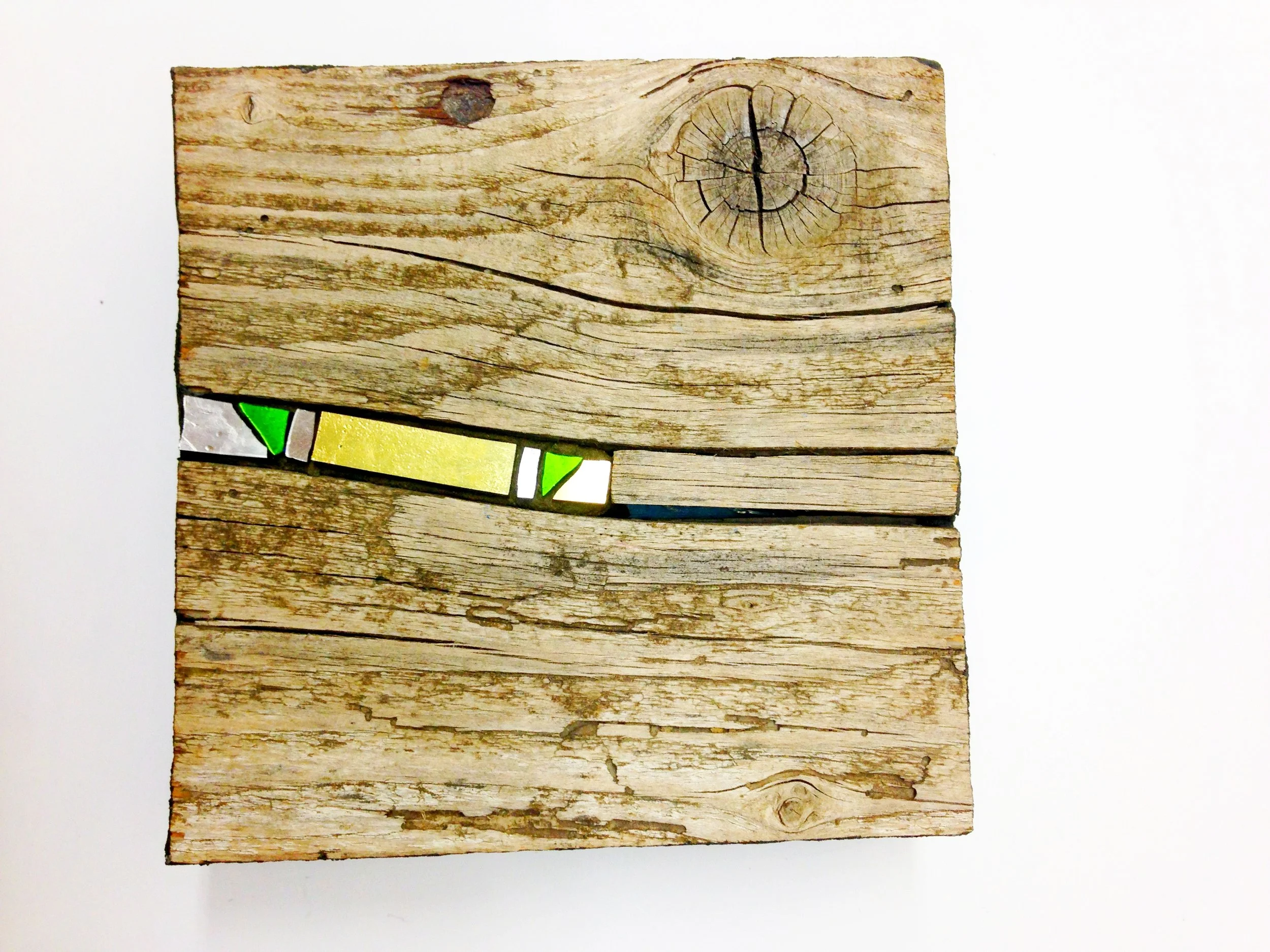 Un morceau de bois rustique avec une mosaïque incrusté colorée avec des triangles verts, jaunes et blancs. Le fond est blanc.