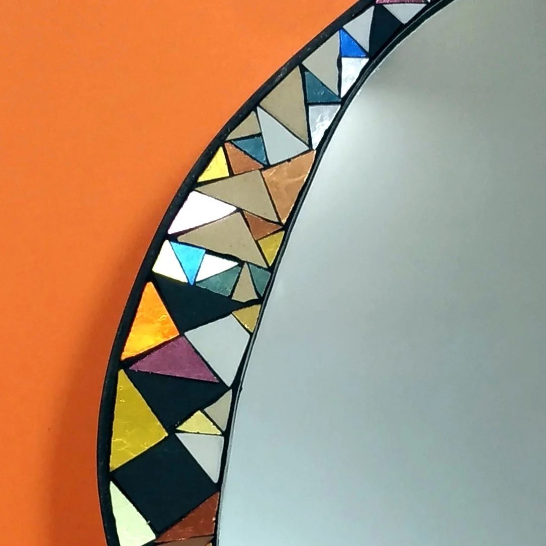 Miroir avec cadre en mosaïque de verre coloré, contre un mur orange.