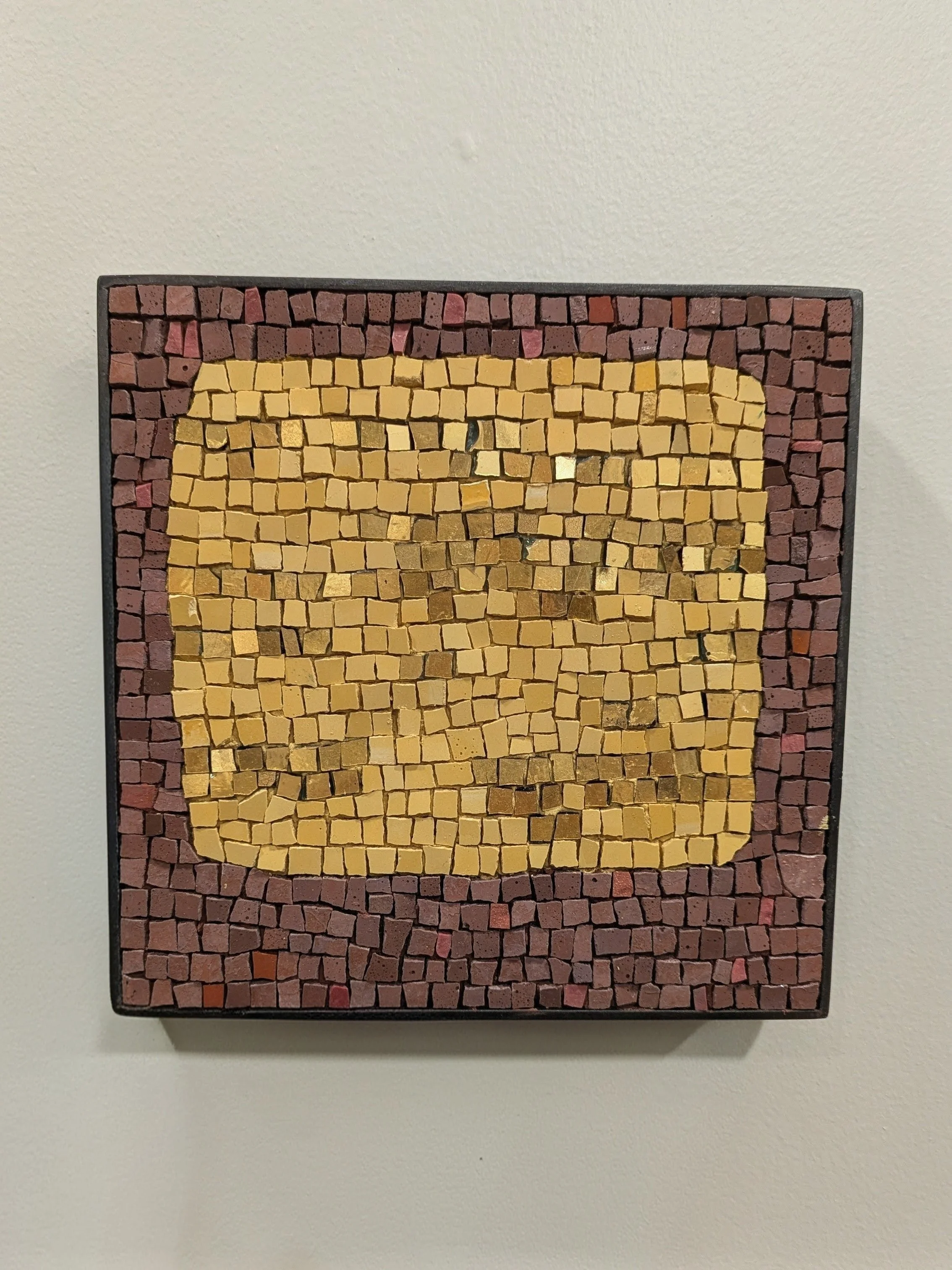 Tableau en mosaïque composé de petites briques colorées en rouge, jaune et or. 