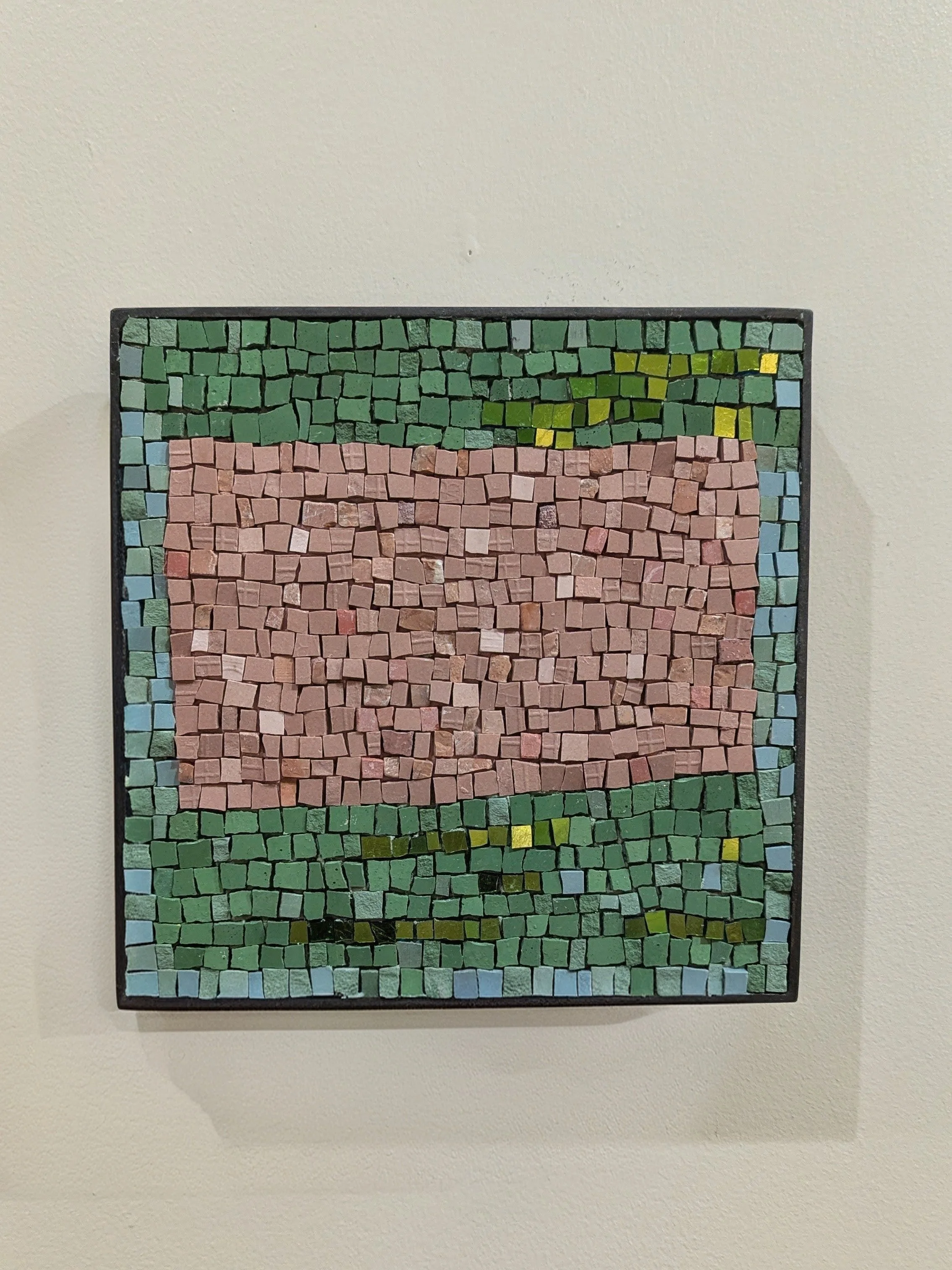 Mosaic en pierre avec une section rose au centre, encadrée par un cadre noir, suspendue sur un mur blanc.
