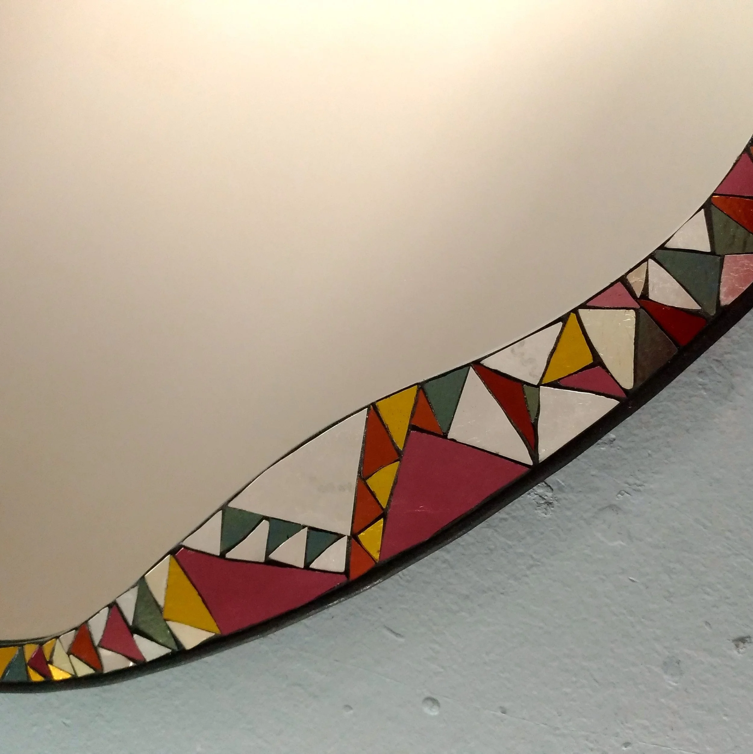 Détails d'un miroir en mosaïque colorés, principalement en rouge, jaune, vert, et orange, dessinés de manière stylisée dans un motif triangulaire.
