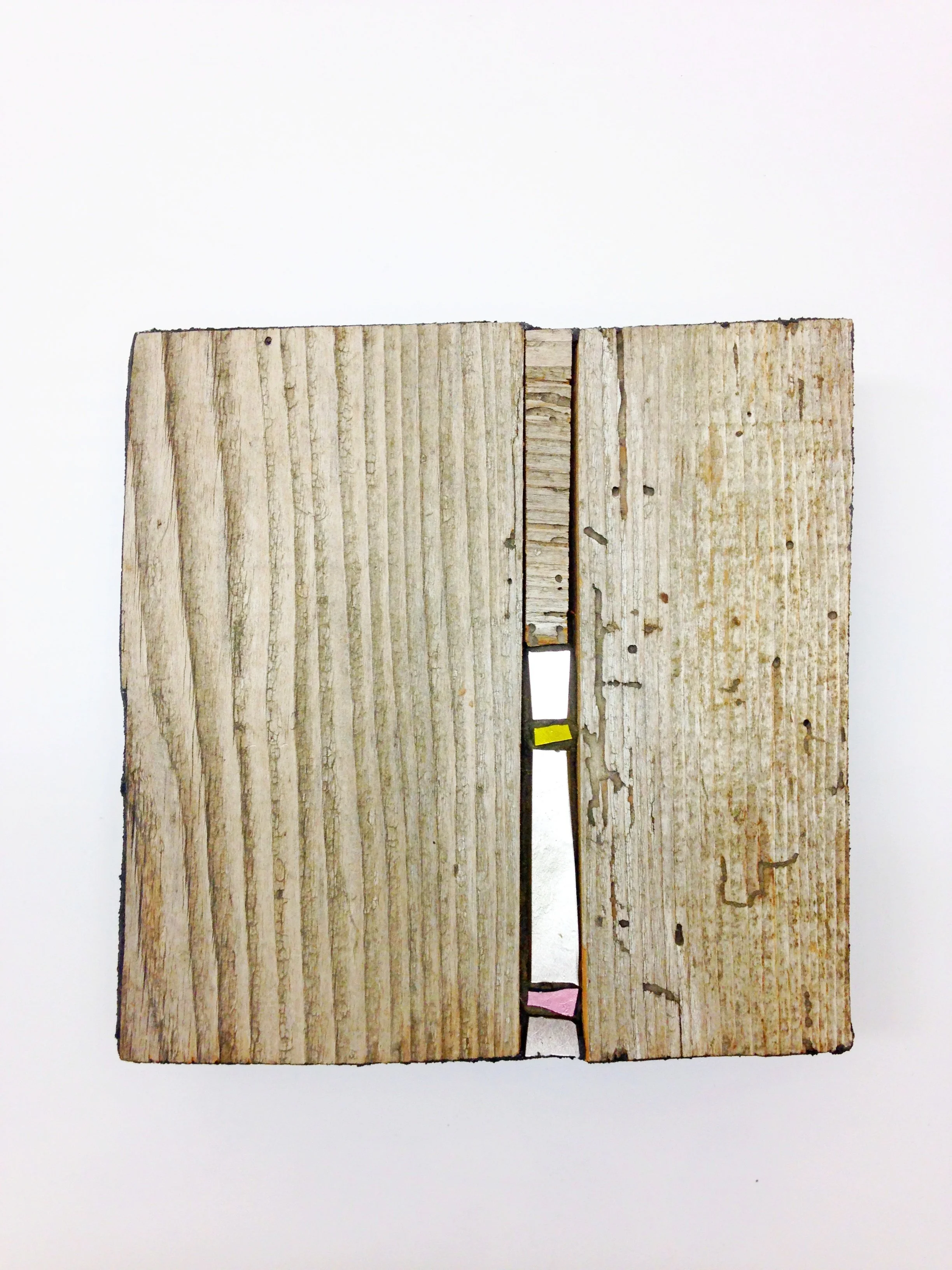 Bijoux muraux en mosaïque. Deux morceaux de bois vieux empilés verticalement avec un espace entre eux, dessus une petite bande de papier rose en bas et un petit morceau de papier jaune en haut à droite.