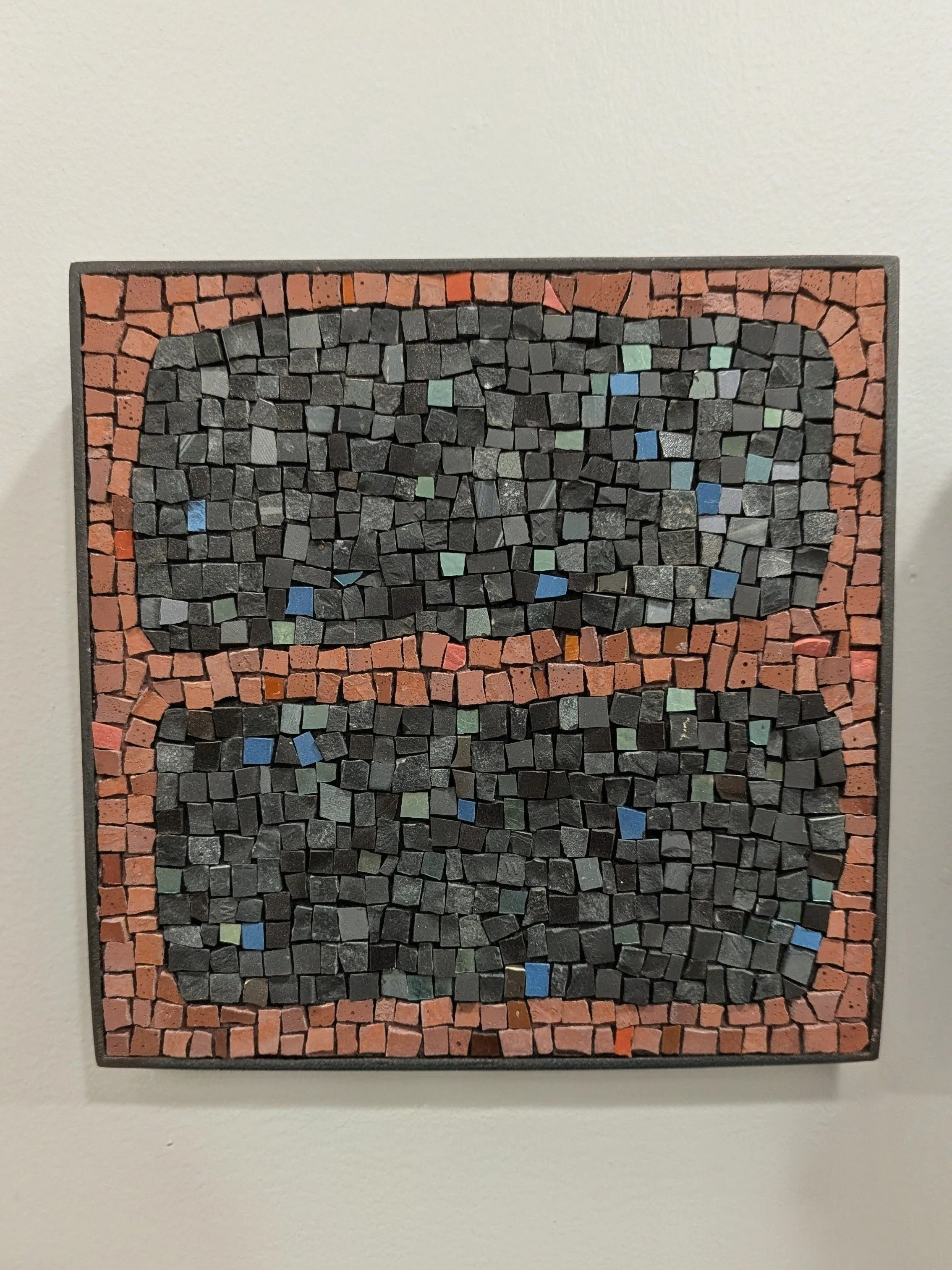 Une mosaïque de petits morceaux de pierre noire, encadrée par une bordure de petits carreaux de pierre rouge.