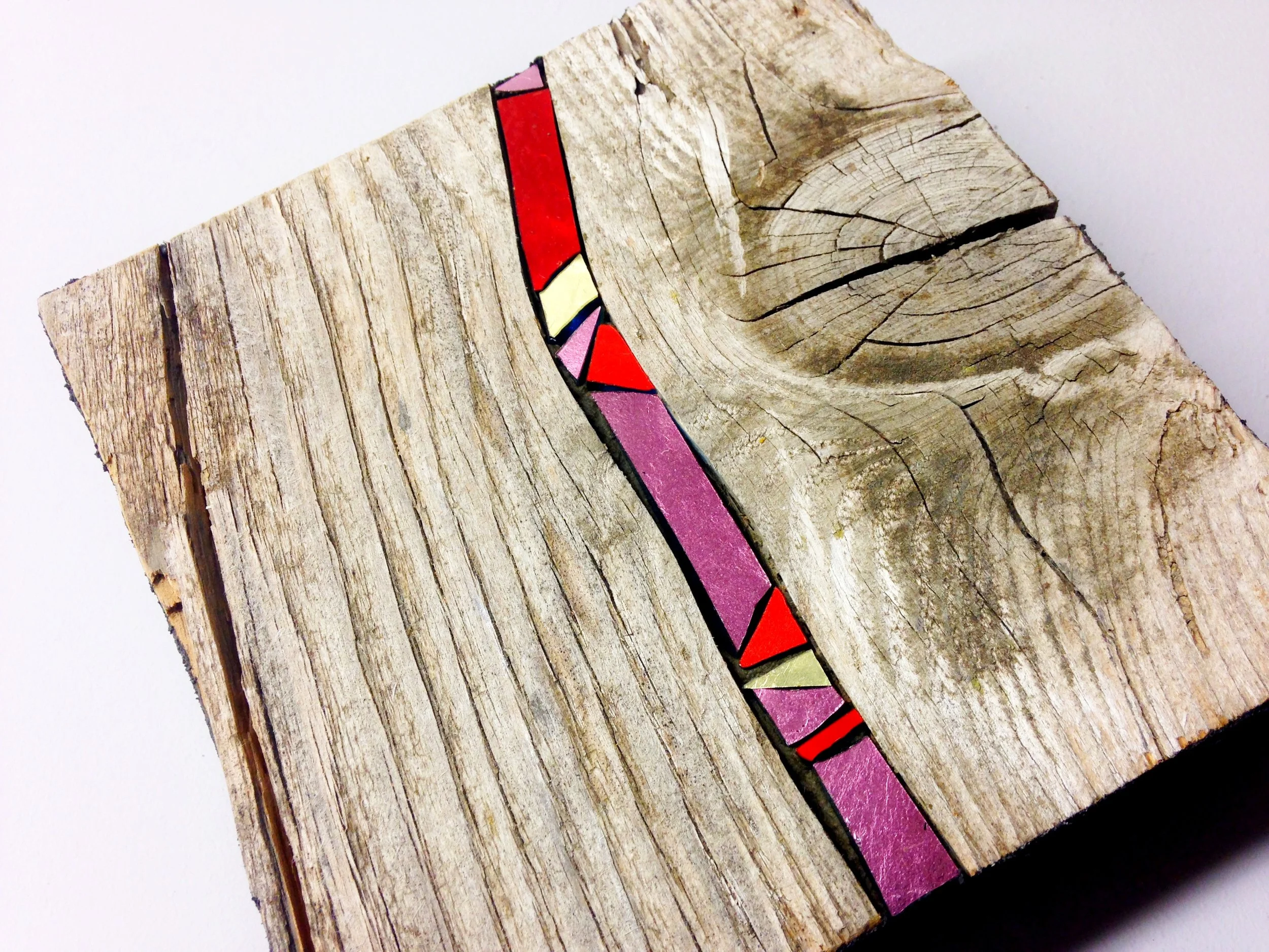 Une pièce en bois avec des motifs colorés incrustés dans une ligne noire. La surface du bois a des fissures et une texture rugueuse.