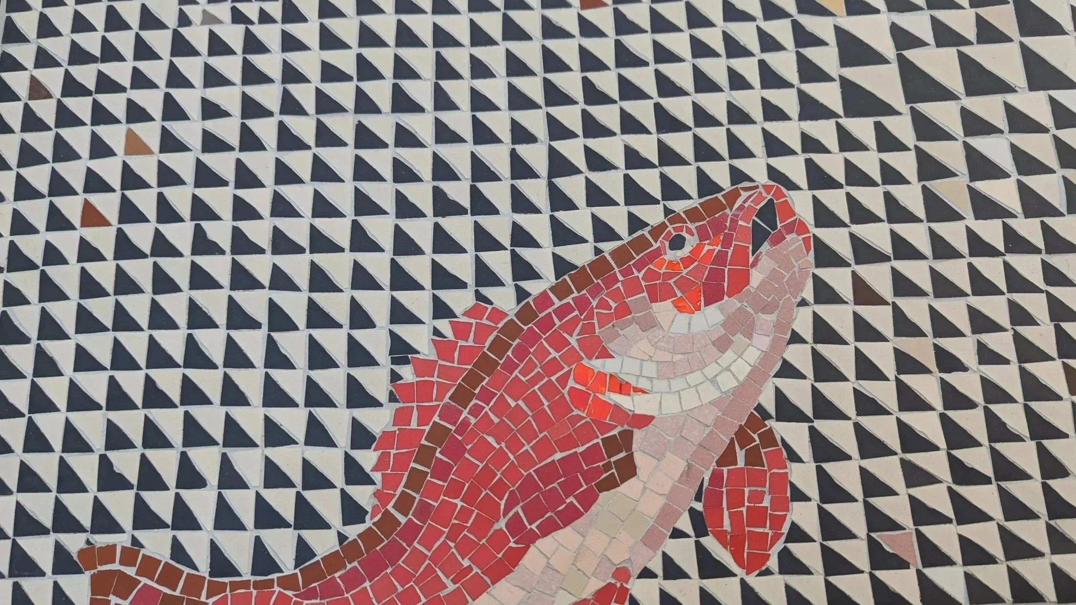 Mosaïque représentant un poisson rouge sur un fond de forme géométrique en noir, blanc et quelques touches de marron