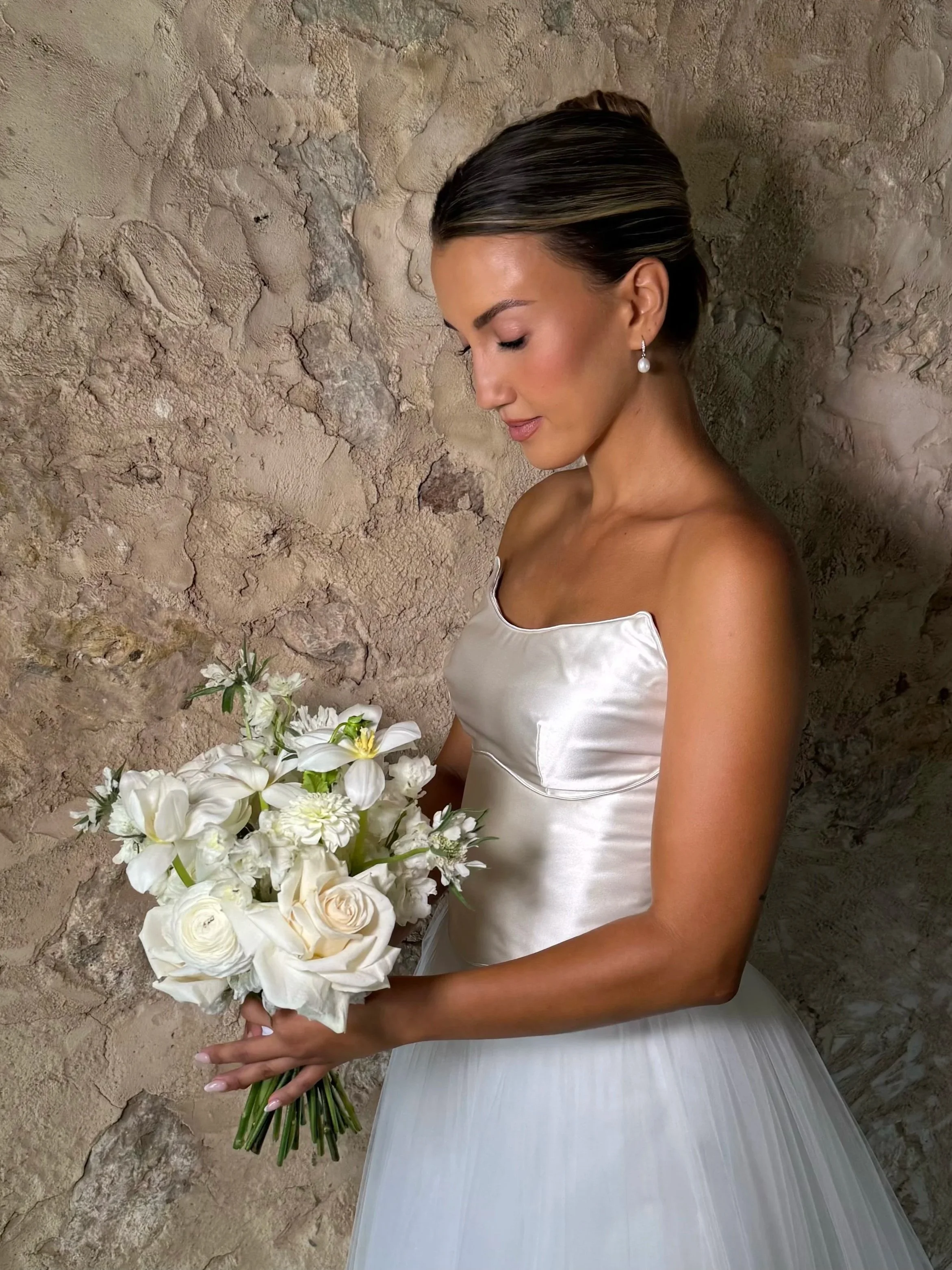 Bride holding a white bouquet against a stone wall before her wedding ceremony
