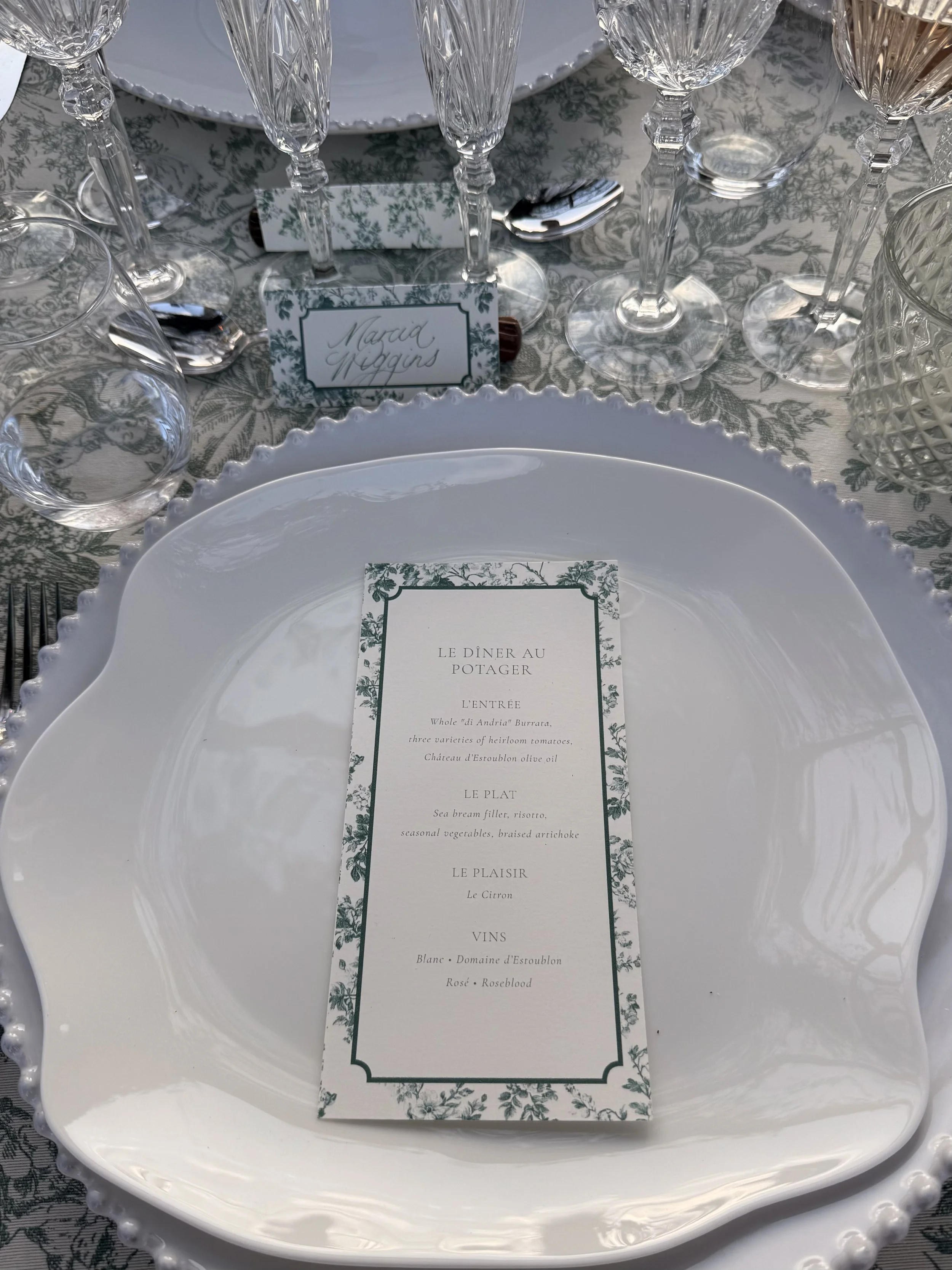 Elegant table setting with crystal wine glasses, a white plate with scalloped edges, and a menu card
