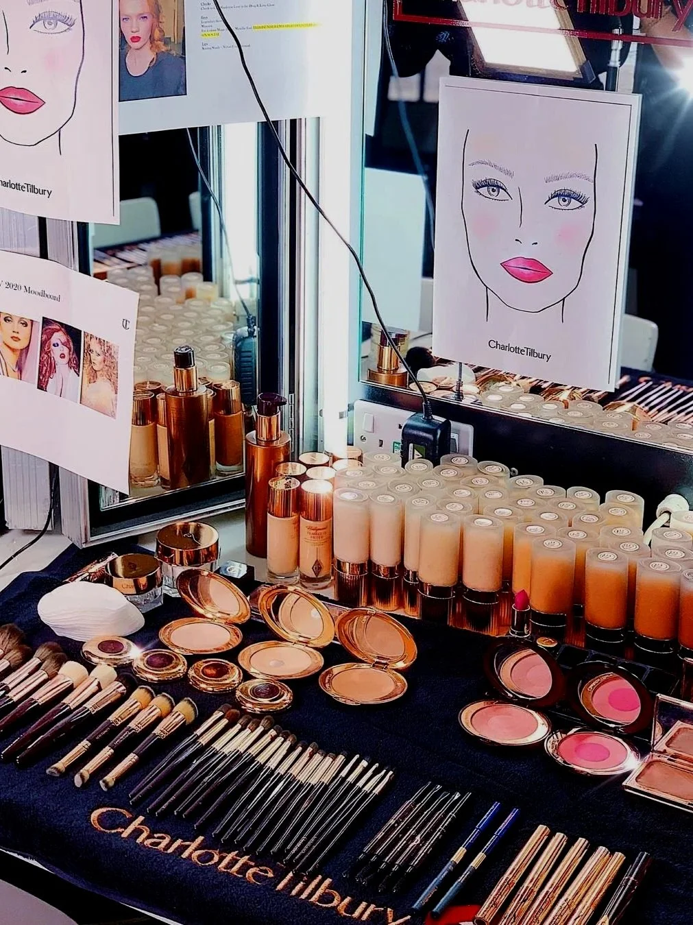 Makeup display with foundation bottles, makeup brushes, and face sketches by Charlotte Tilbury at a beauty booth.