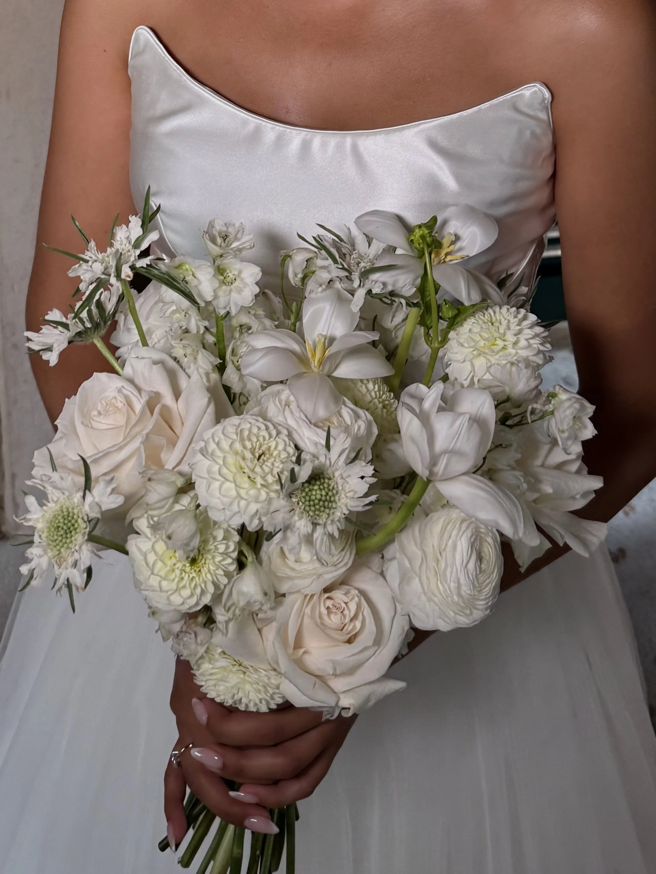 A bride dressed in a white satin dress holding a bouquet of white flowers.