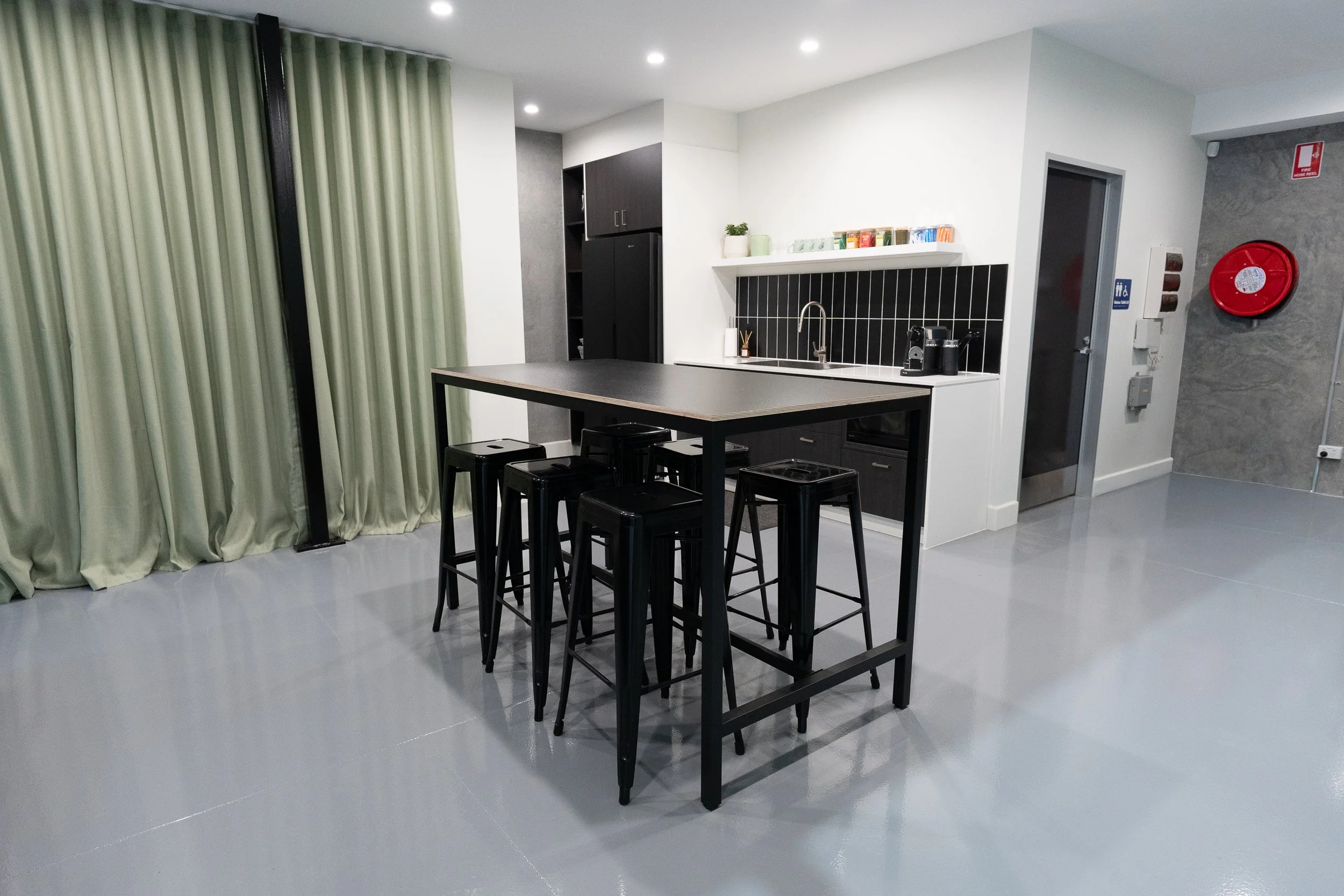 A modern interior scene featuring a gray concrete wall, a white sofa, green and gray chairs, a wooden coffee table, potted plants, and professional lighting equipment in a creative studio.