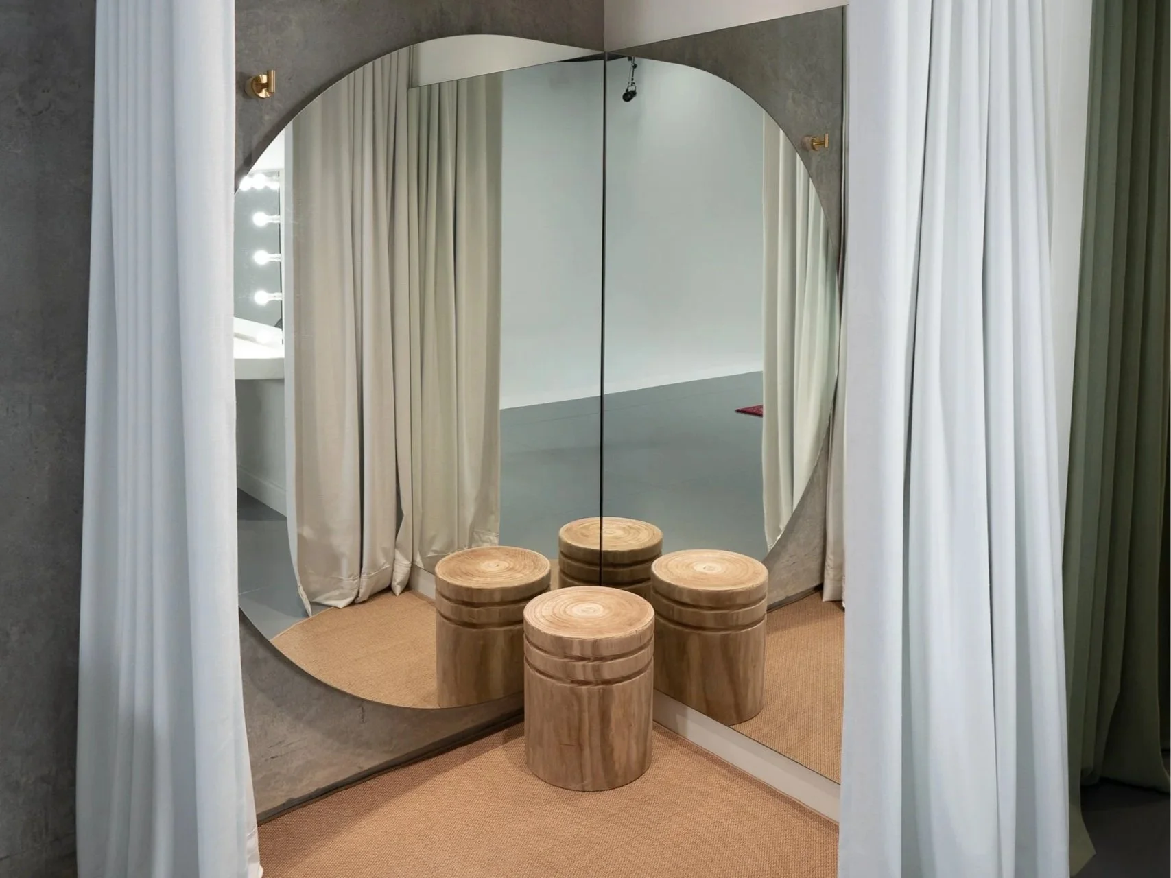 Decorative mirror with wavy edges and a plant with large green leaves reflected in it, seen through sheer white curtains.