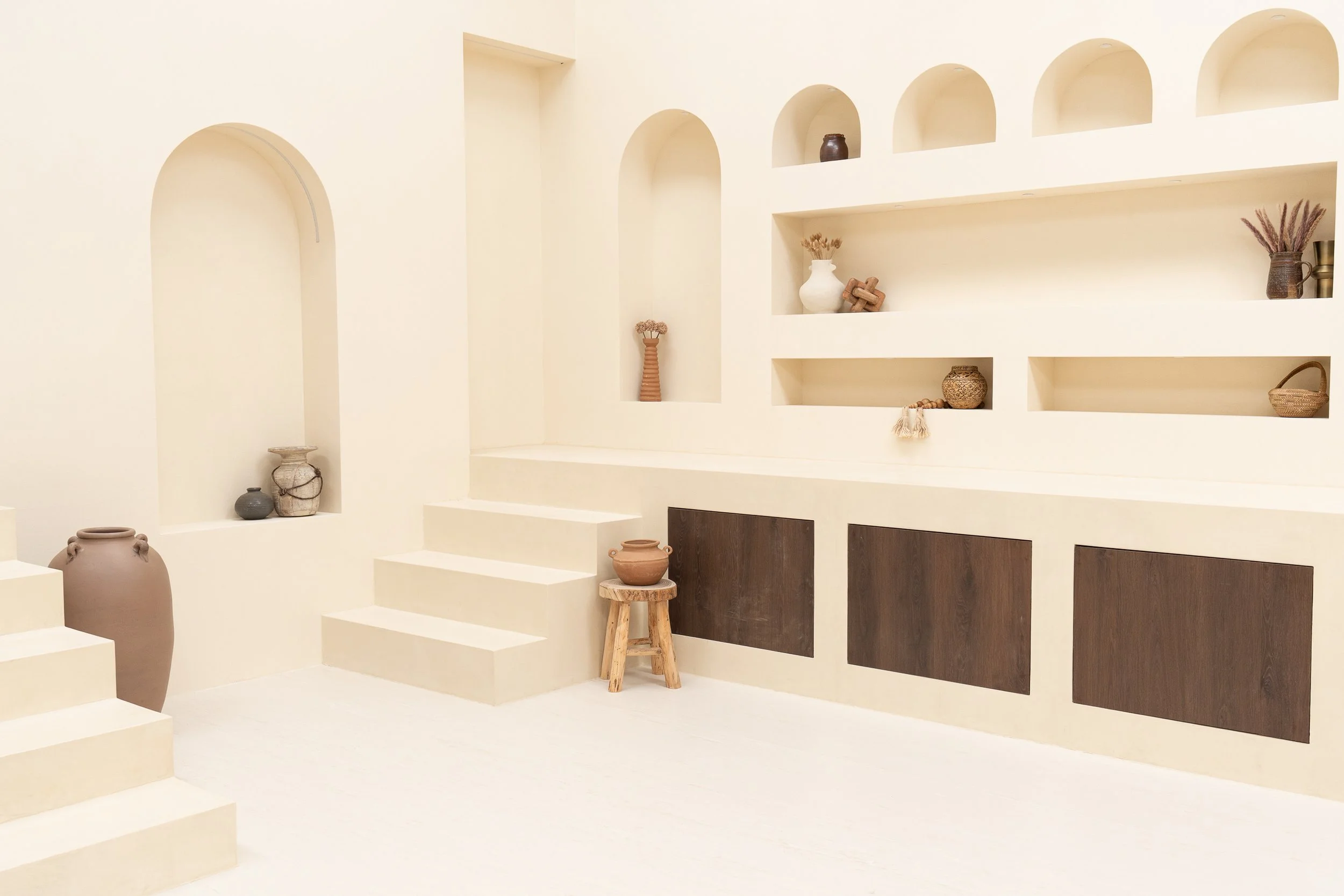 Minimalist beige room with built-in bench seating and decorative alcoves, including vases and small sculptures.