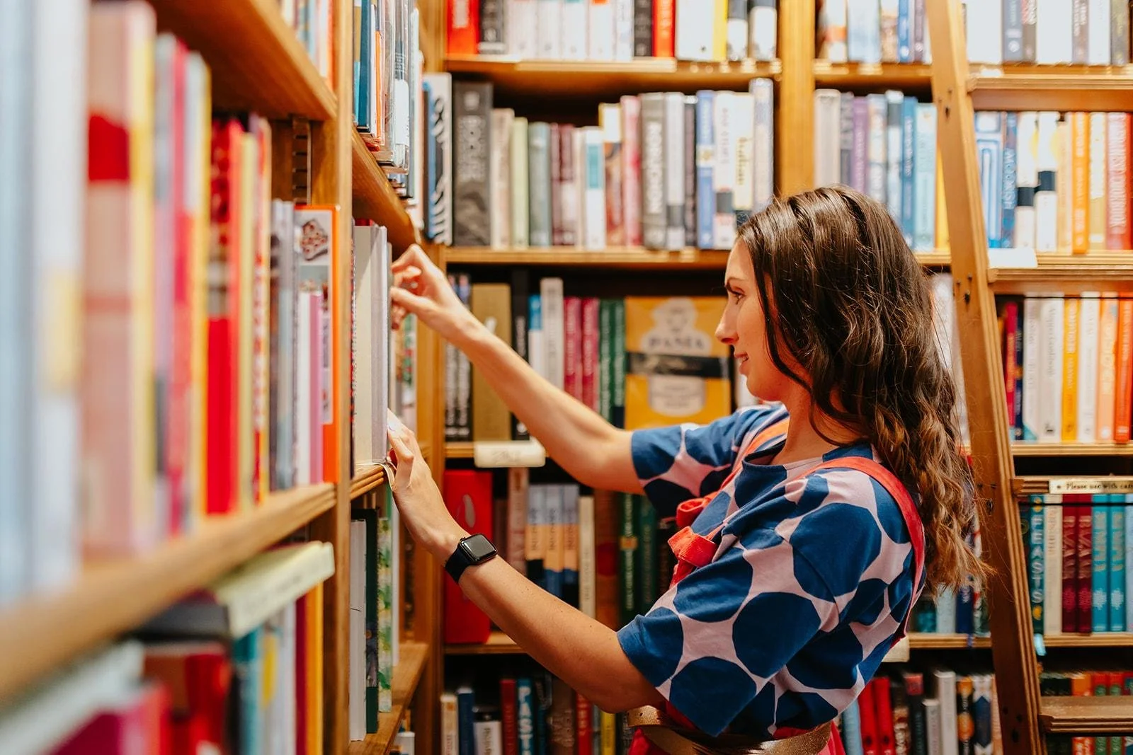 Chloe wearing a blue patterned shirt shopping for books in a bookstore.