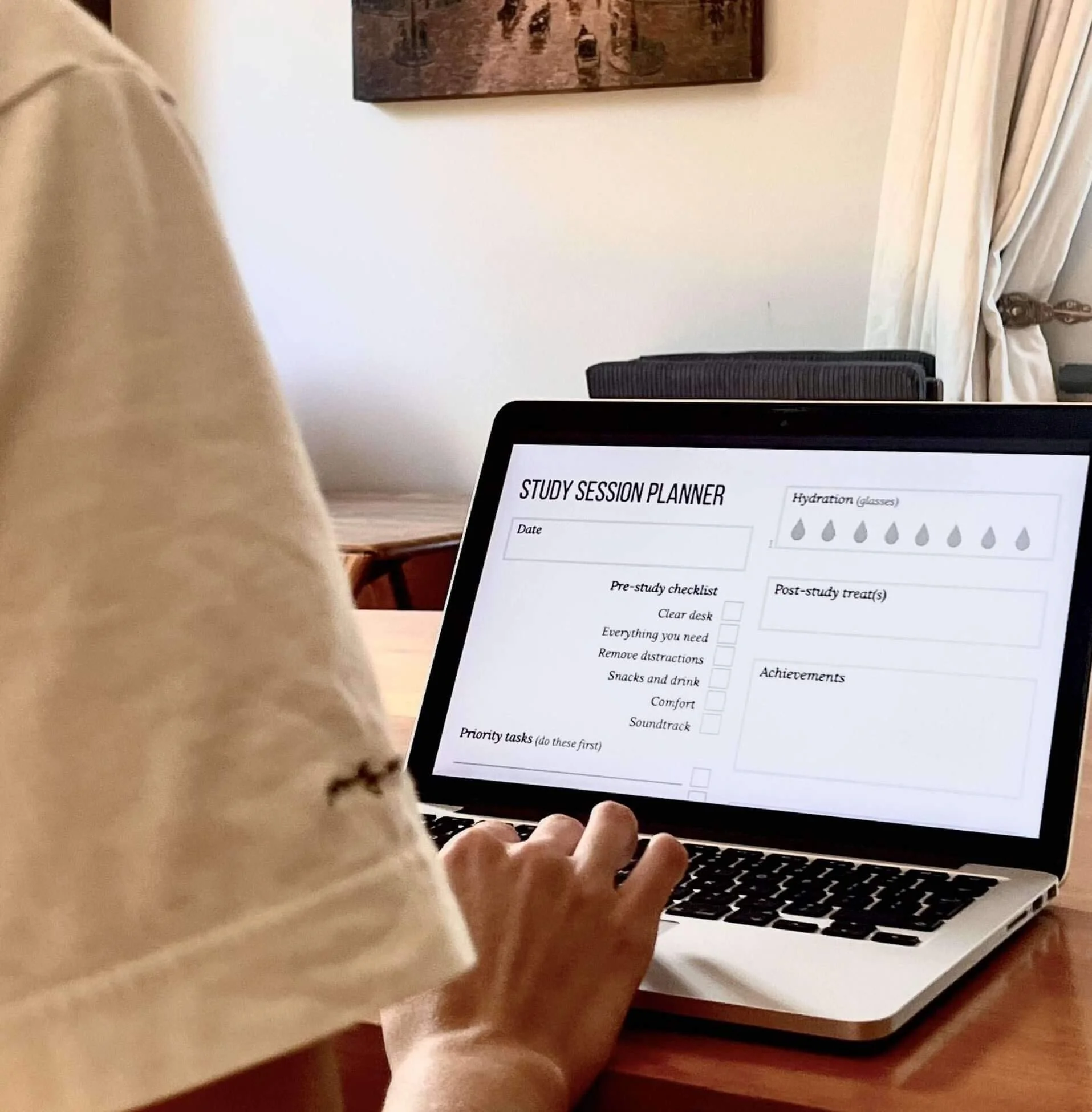 Person working on a laptop with a study session planner on the screen, placed on a wooden table, with cream-coloured curtains and a framed painting in the background.