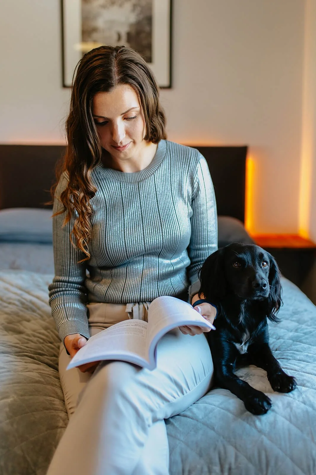 Chloe sitting on a bed with a black dog beside her, reading her Return to Study Handbook.