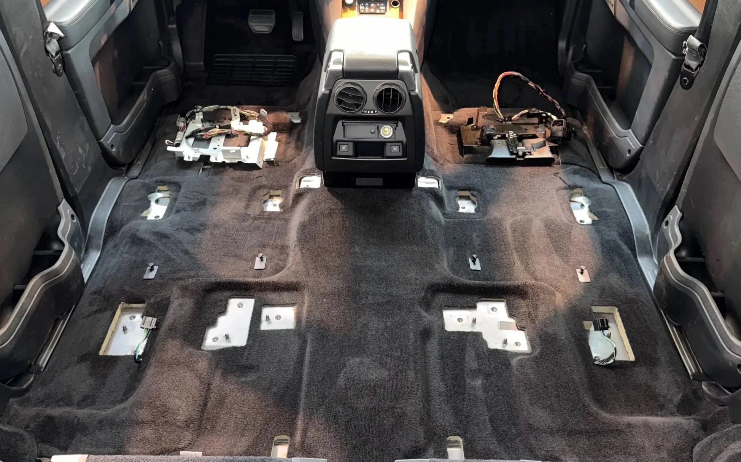 The interior of a car with the seats removed, showing the exposed floor and wiring, with some components and wiring harnesses placed on the floor. Cleaned interior