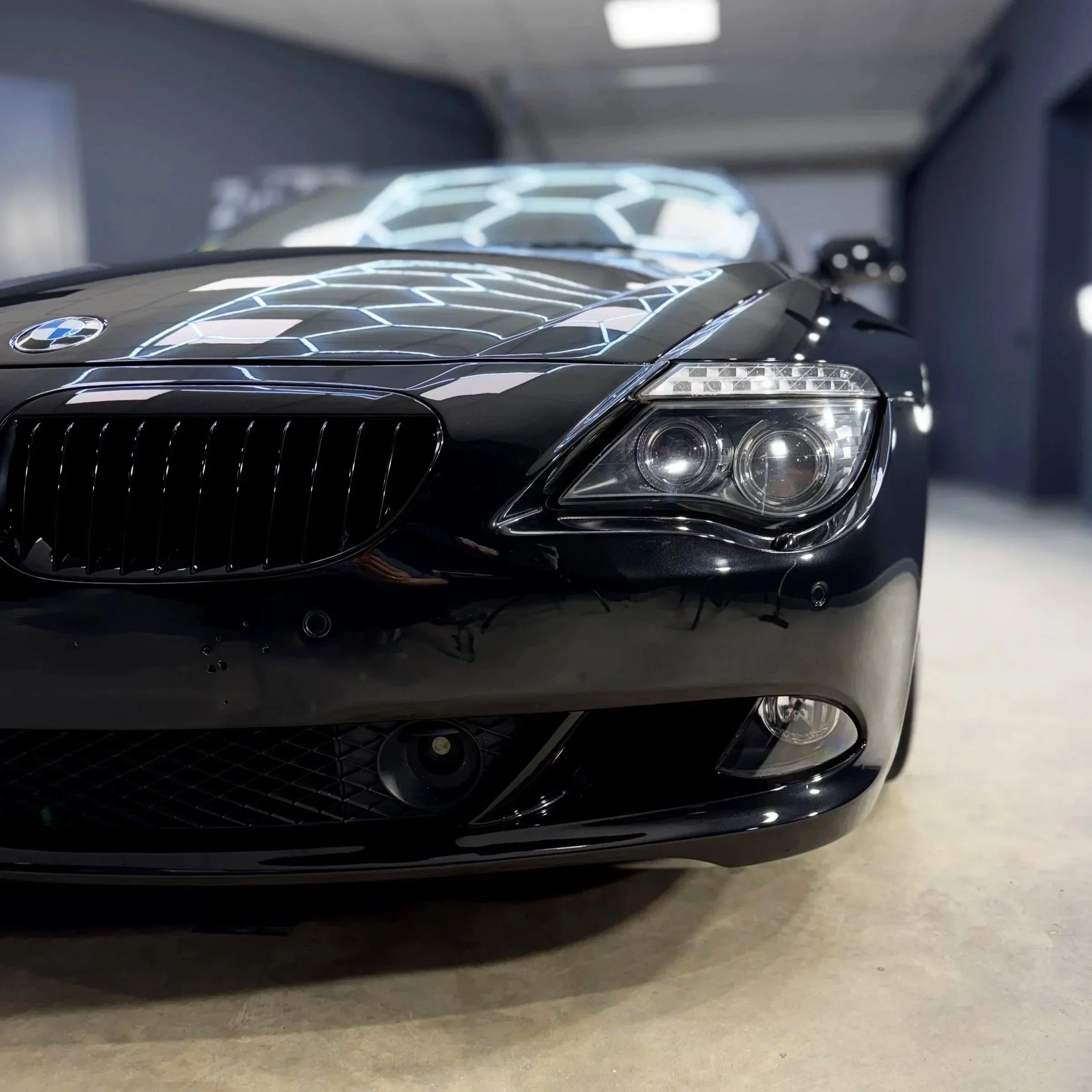 Close-up of the front of a black BMW car with a reflective glossy finish and decorative illuminated hood design. 3 stage polish done