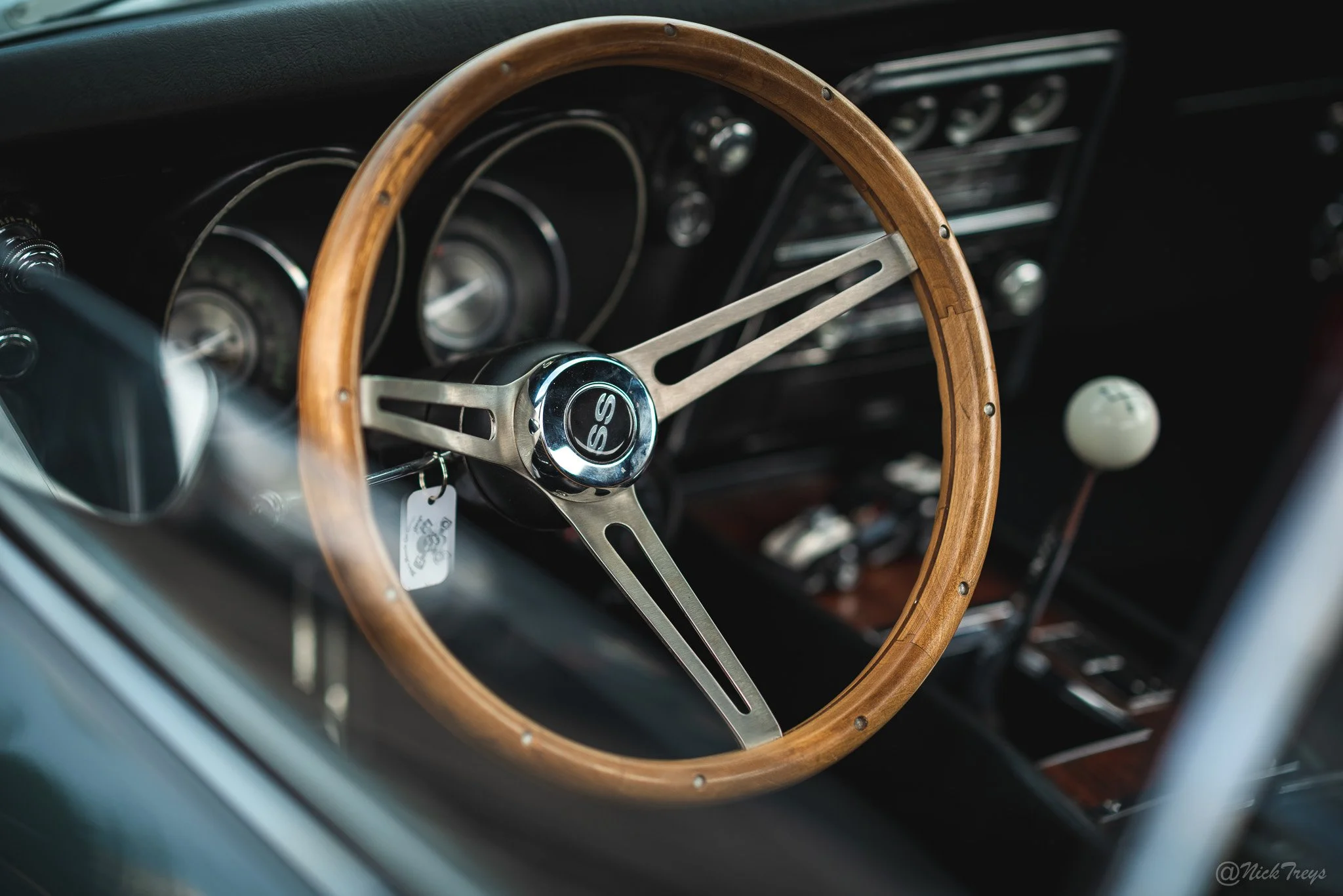 A vintage car interior showing a wooden steering wheel with a chrome center cap and a dashboard with analog gauges.