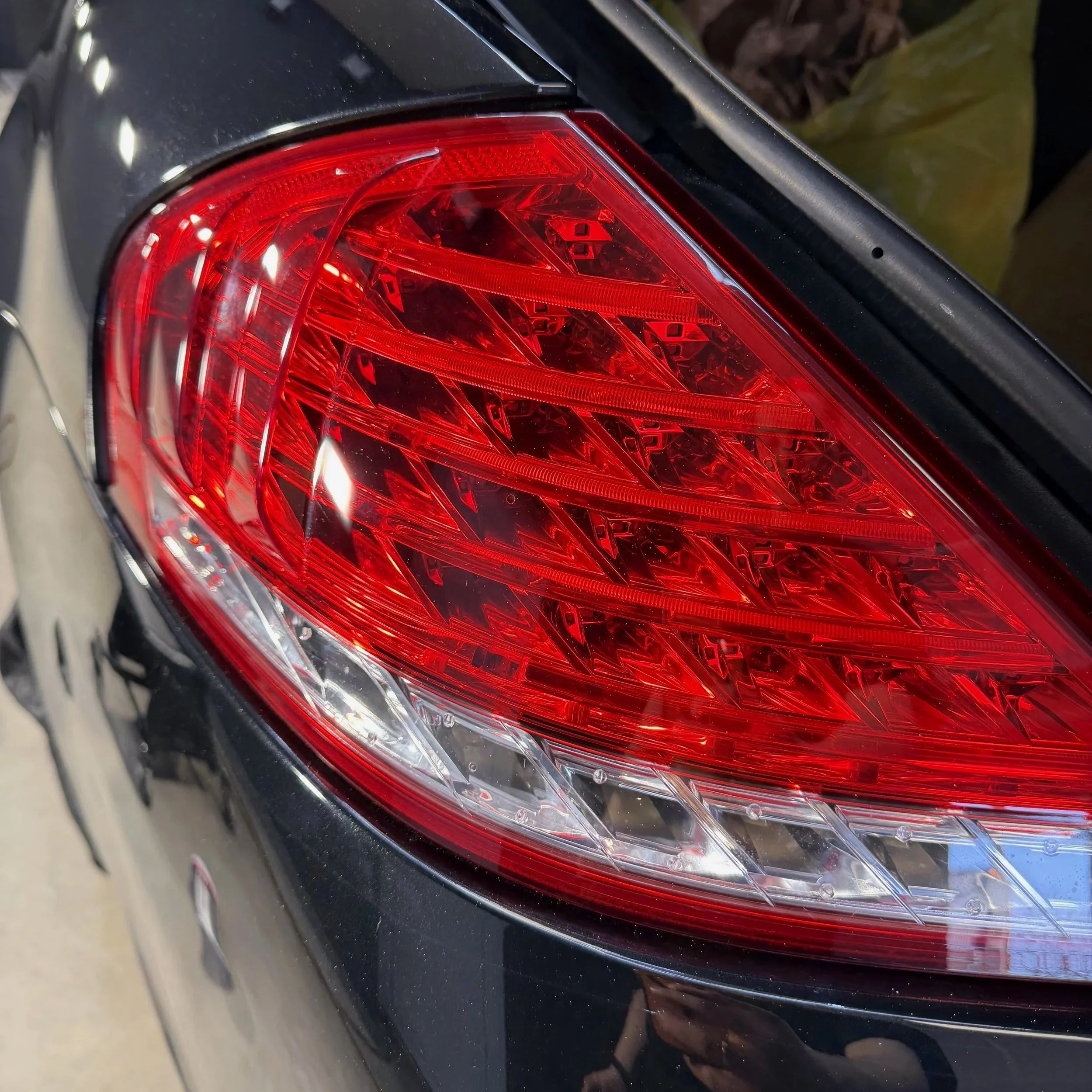 Close-up of a red car taillight on a black vehicle in a parking lot.