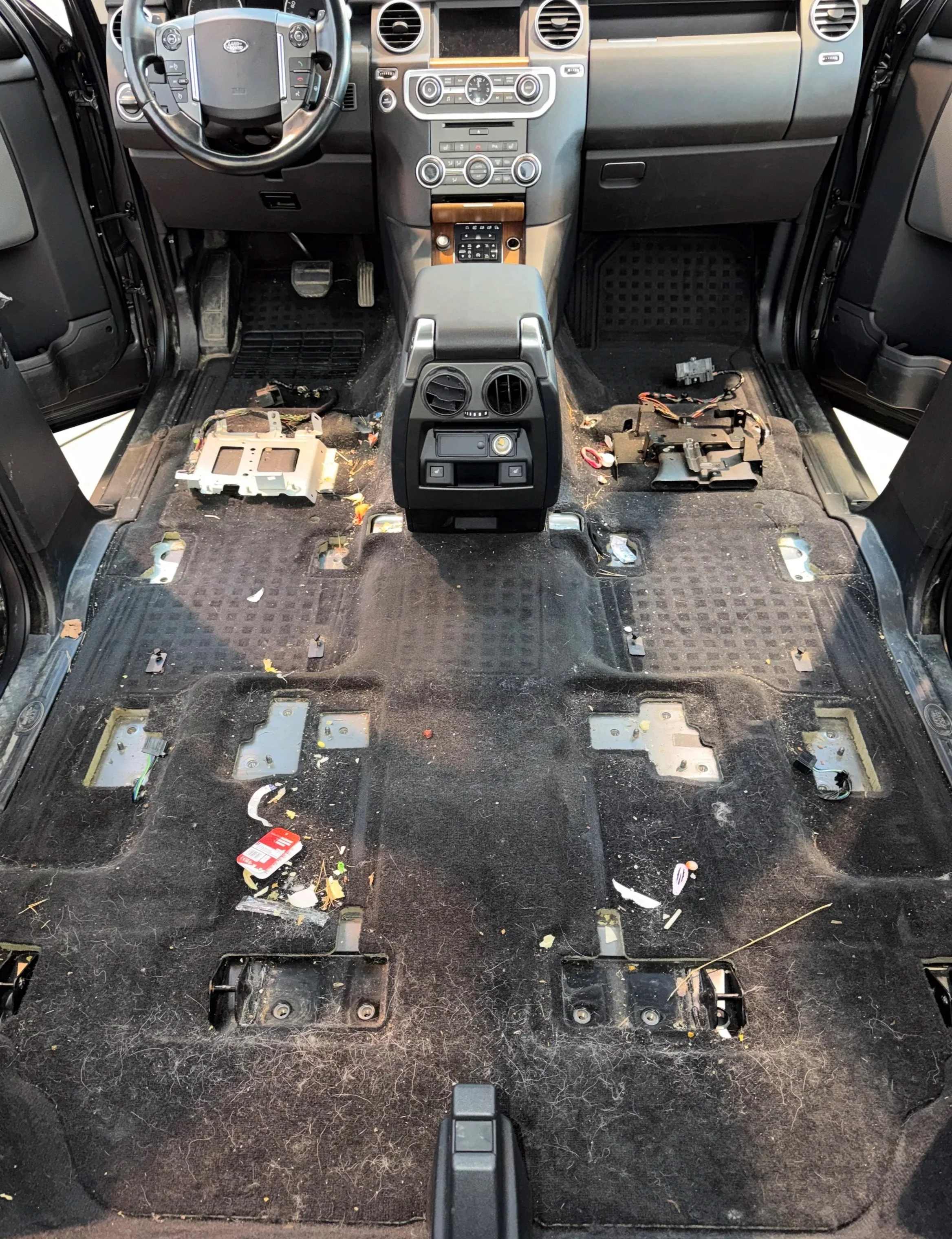 The interior of a vehicle with the seats removed, showing dirt, debris, wires, and electronic components on the floor.