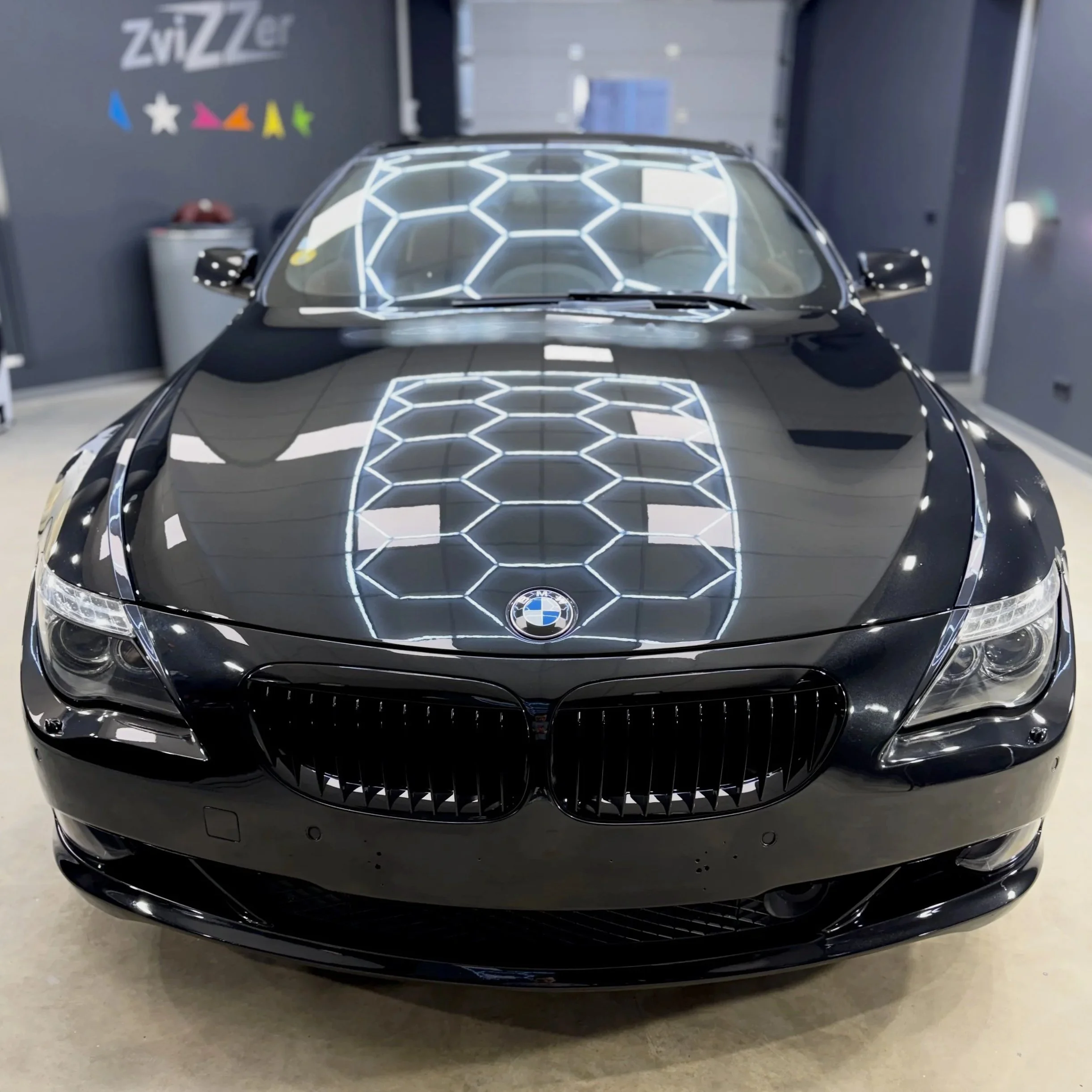 The front view of a black car with a futuristic honeycomb pattern LED light design on the windshield and hood, parked indoors. BMW 6 series