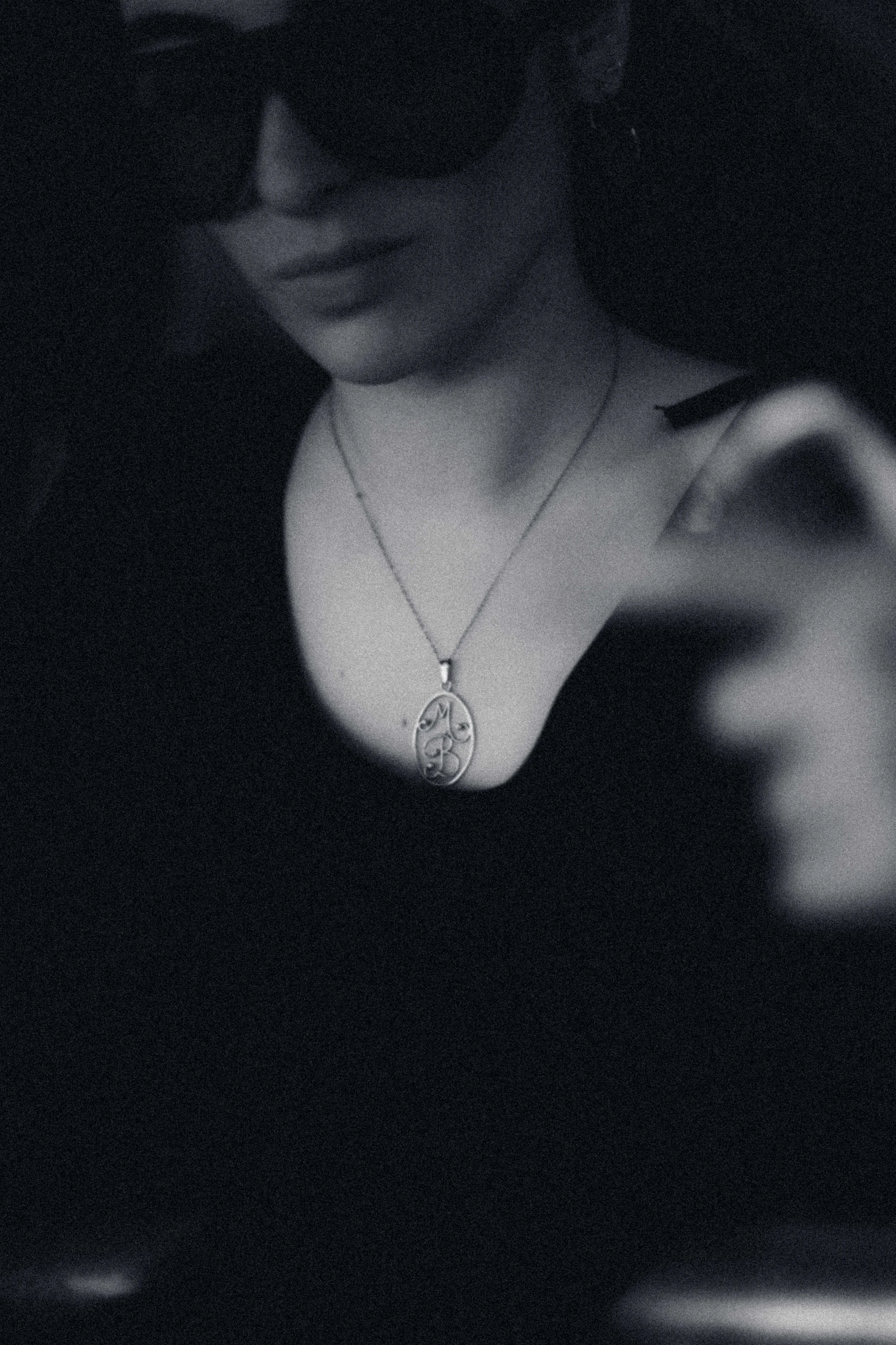 Una donna con cappello nero e occhiali scuri indossa una collana con pendente con le lettere M, B e forse altre, visibile sul seno.