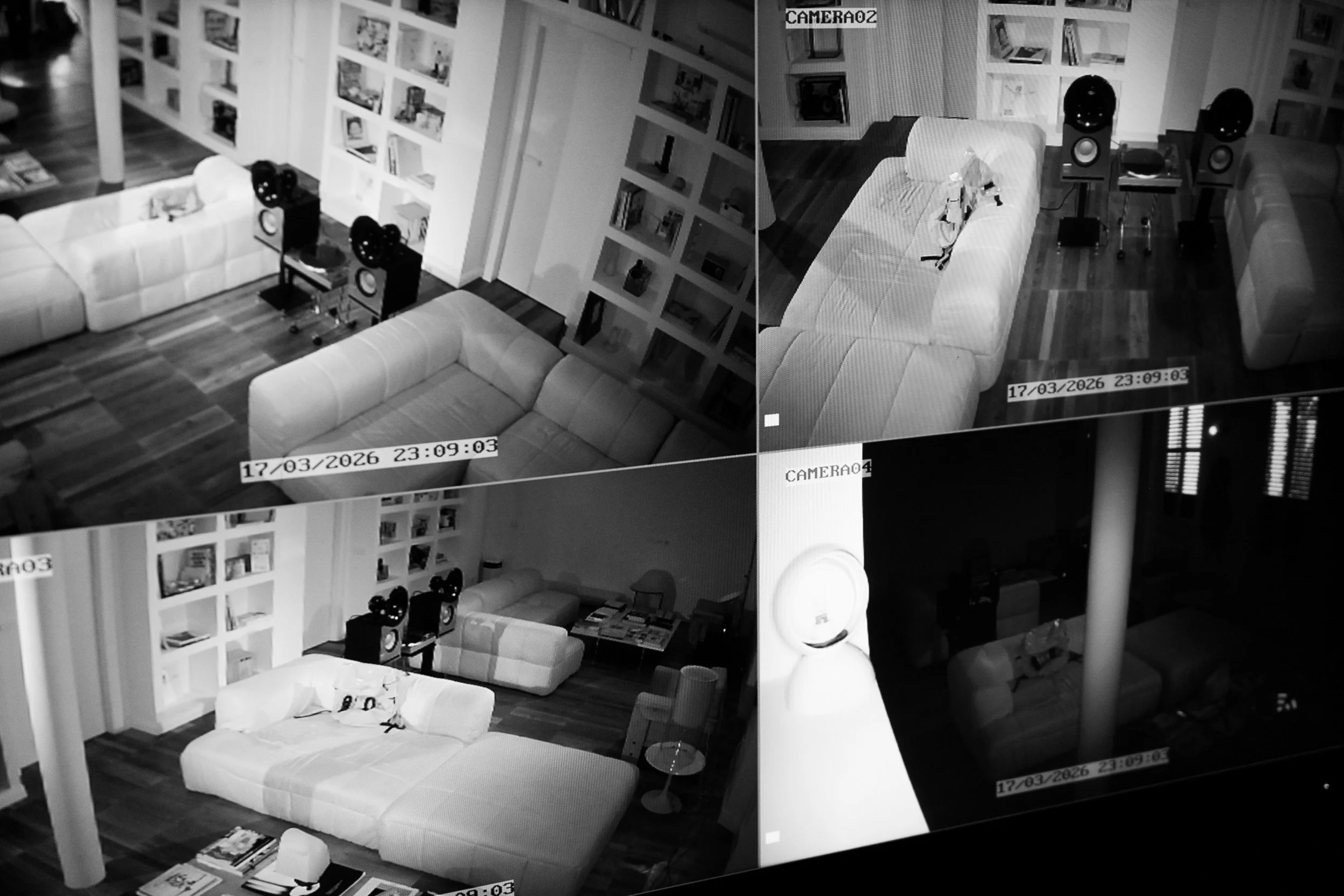 Ripresa di una stanza con divano, stereo e scaffali pieni di libri e oggetti, vista tramite telecamere di sorveglianza