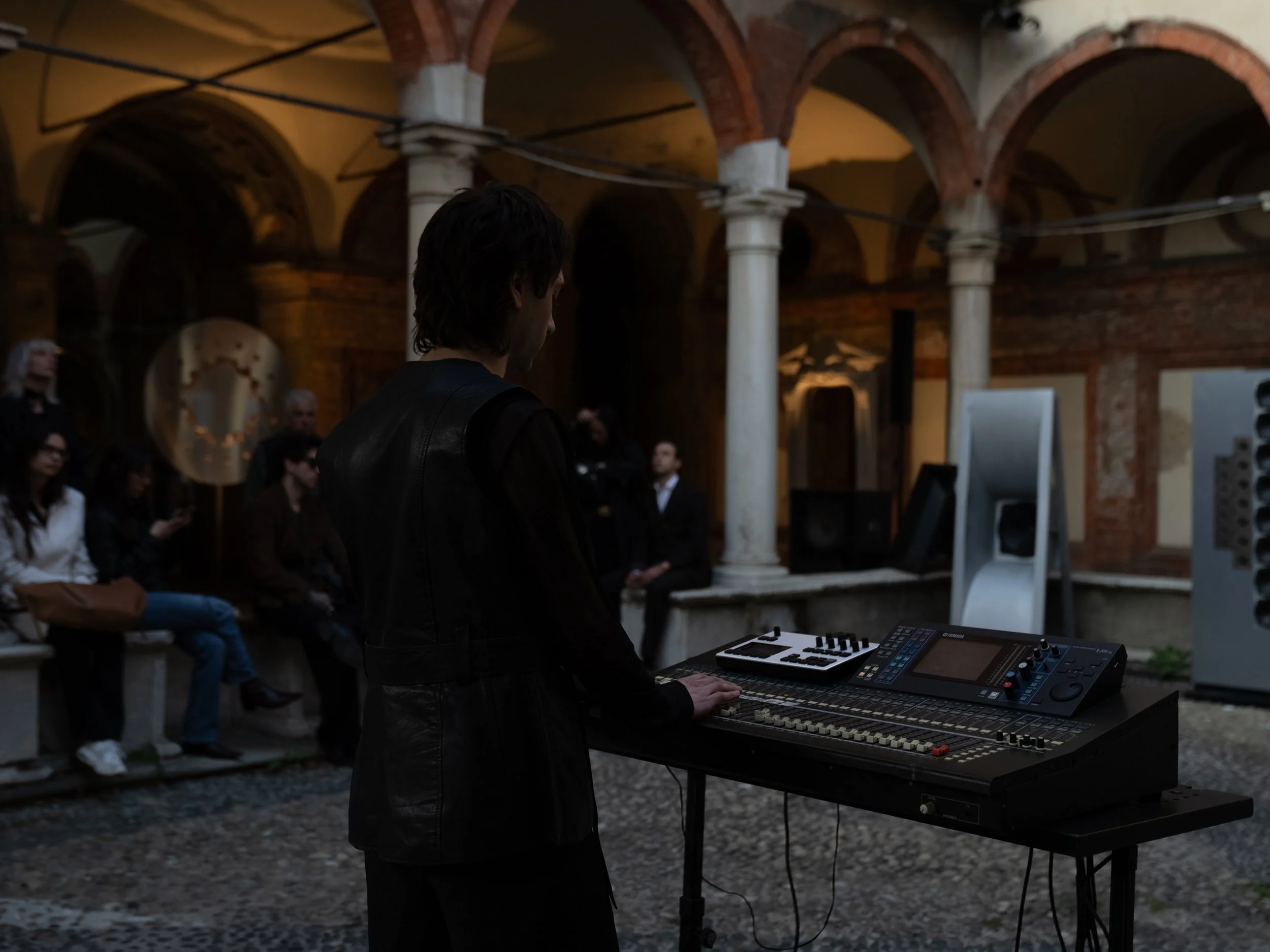 Un musicista sta suonando un sintetizzatore in un ambiente sotterraneo con archi in mattoni e colonne.