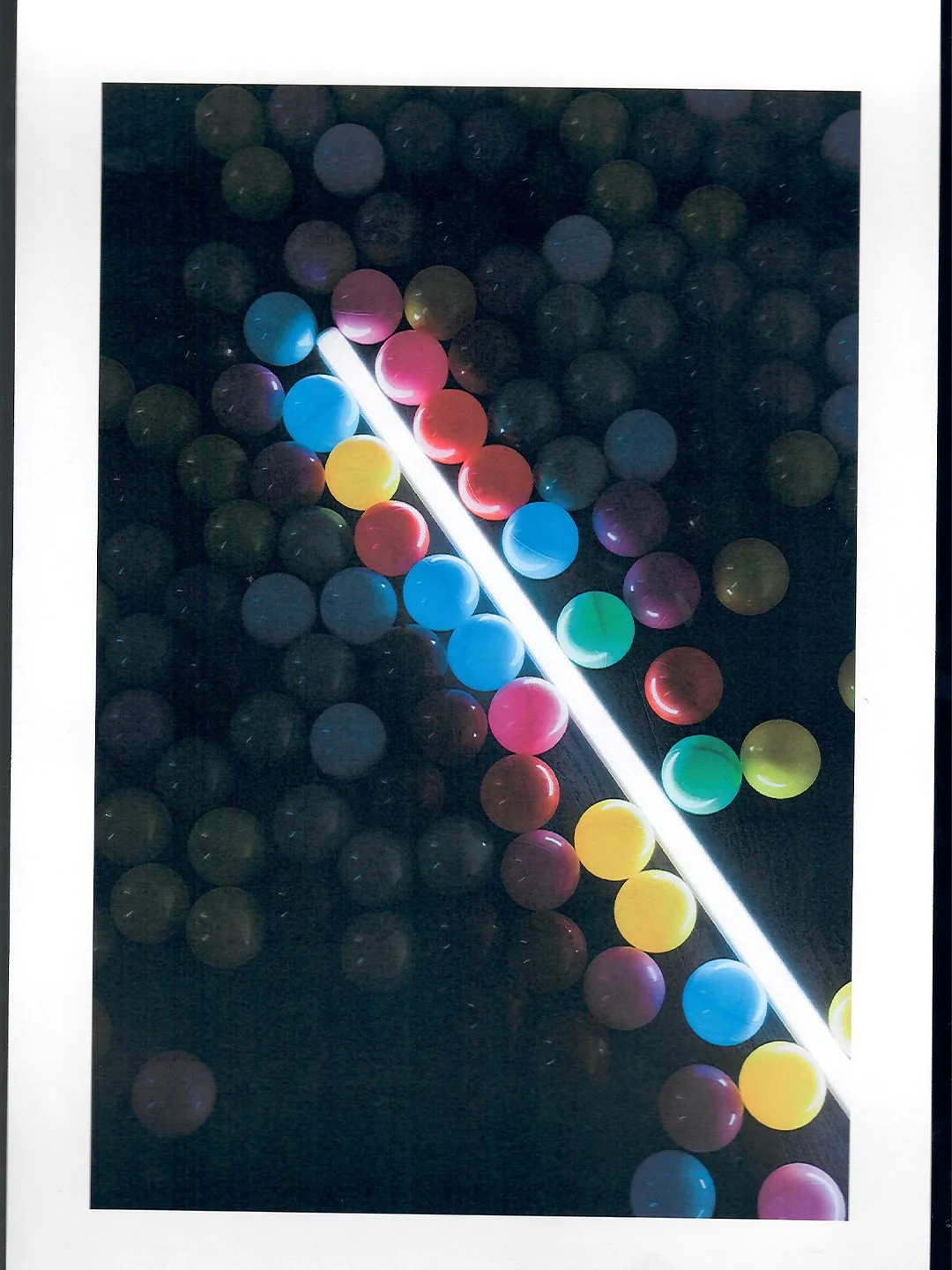 Bolle di vetro colorate distribuite su una superficie scura, con una striscia luminosa bianca che attraversa diagonalmente il centro dell'immagine.