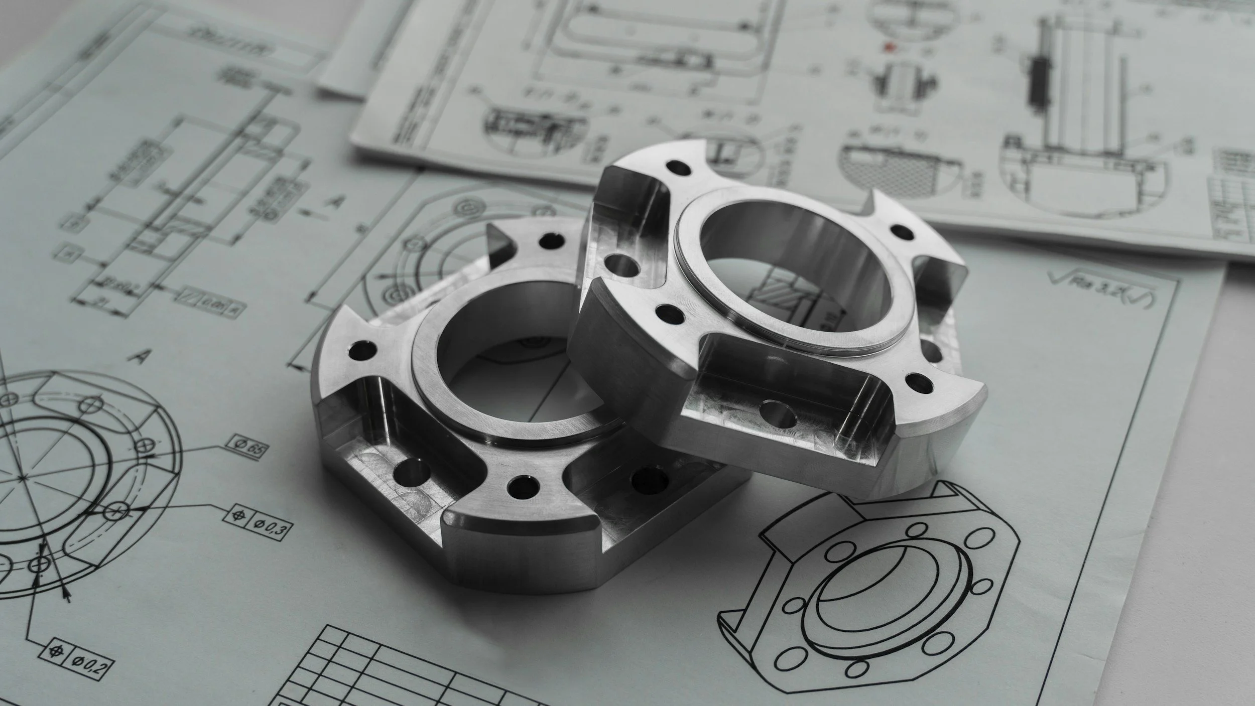 A metallic machined part placed on technical blueprints with engineering drawings.
