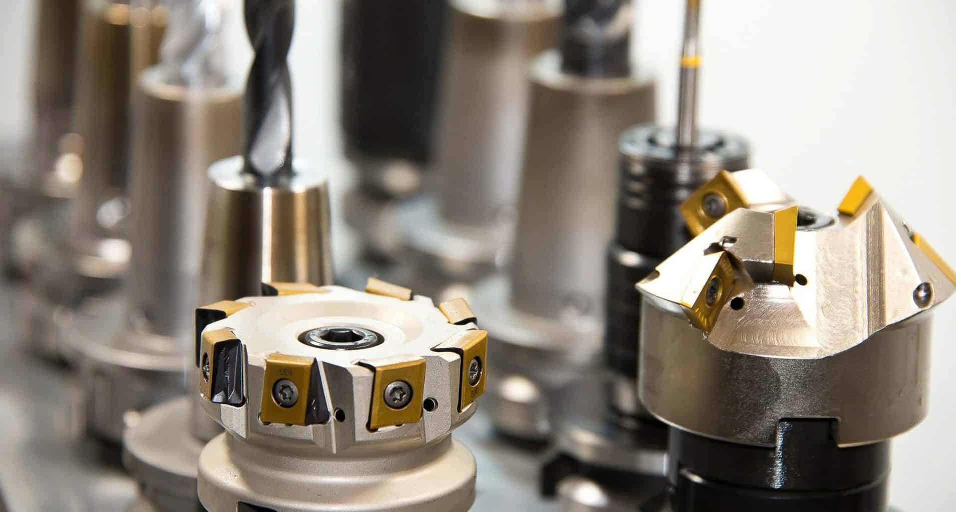 Close-up of multiple metal cutting tools with sharp edges and yellow accents, mounted on machines for machining or manufacturing processes.